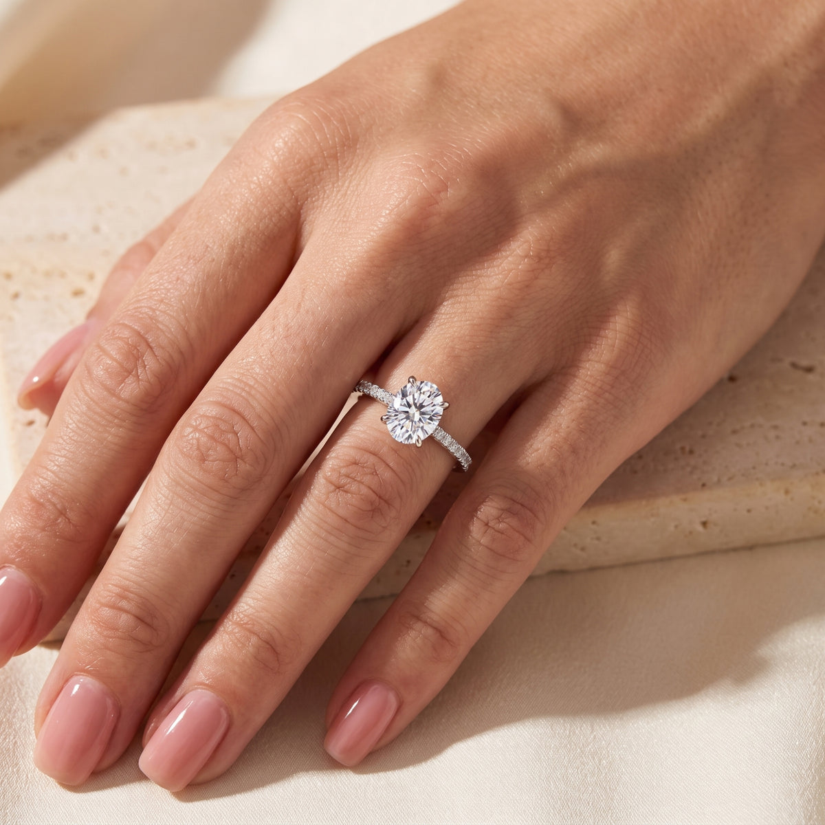 Overhead hand view of the silver ring featuring a clear oval stone set on a pavé-accented band.