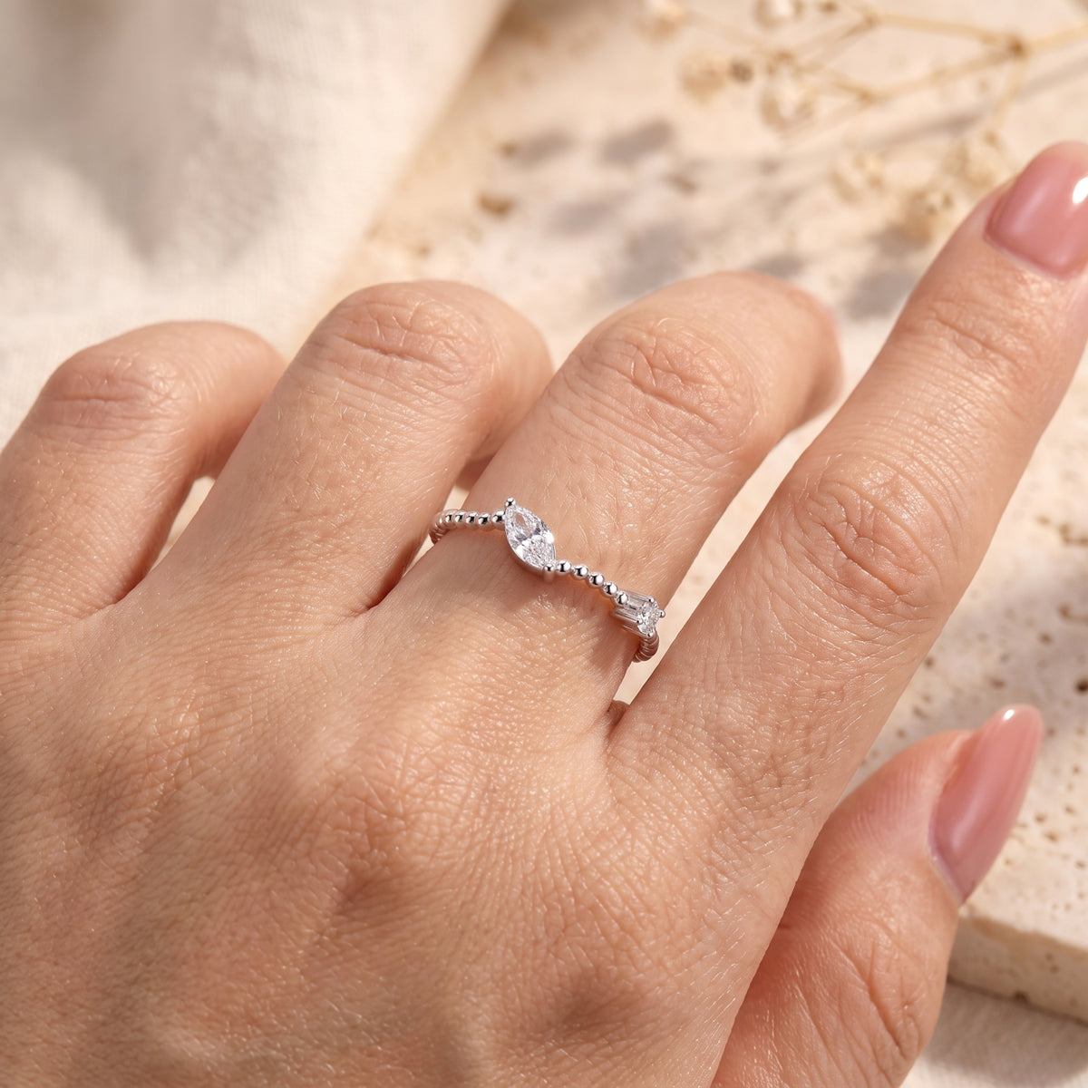 Top view of a hand wearing the silver beaded bypass ring with clear marquise and round stones.