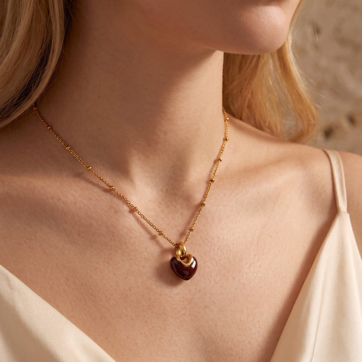 Side view of a woman wearing the gold-tone beaded necklace with a dark red heart pendant over a white top.