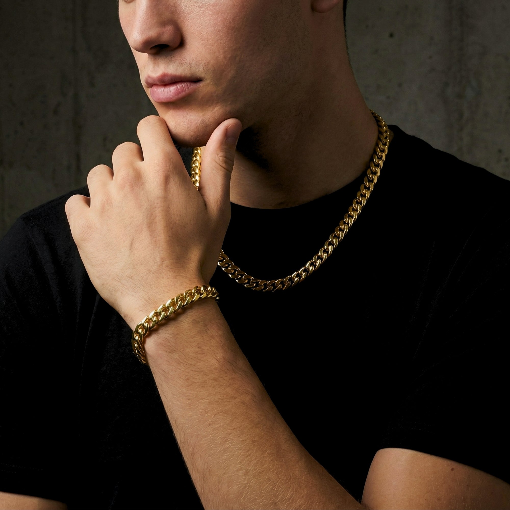 Model wearing a 10mm gold stainless steel Cuban link chain and bracelet set, hand resting on chin.