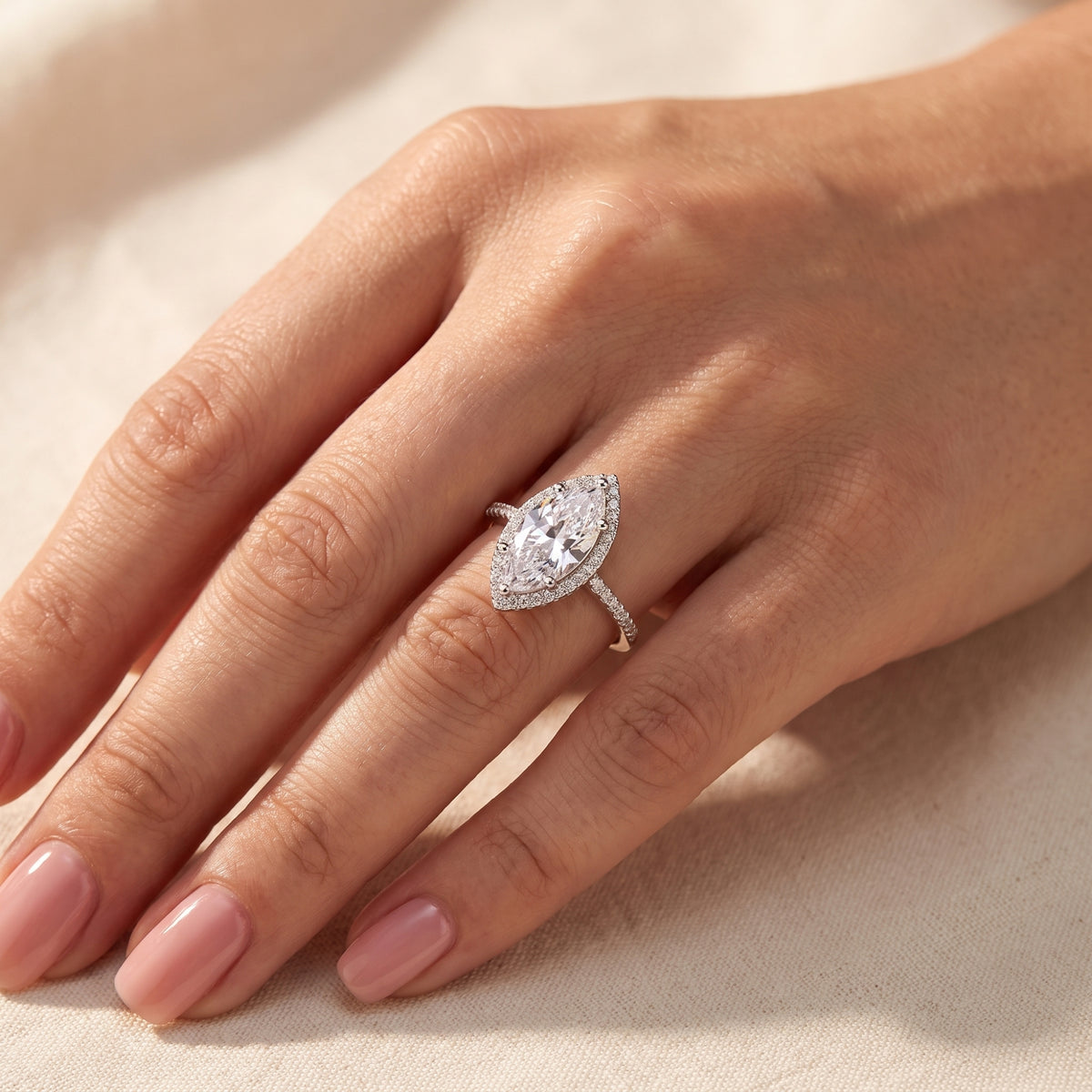 Top-down hand view of the silver marquise-cut halo ring worn on a finger against neutral fabric.