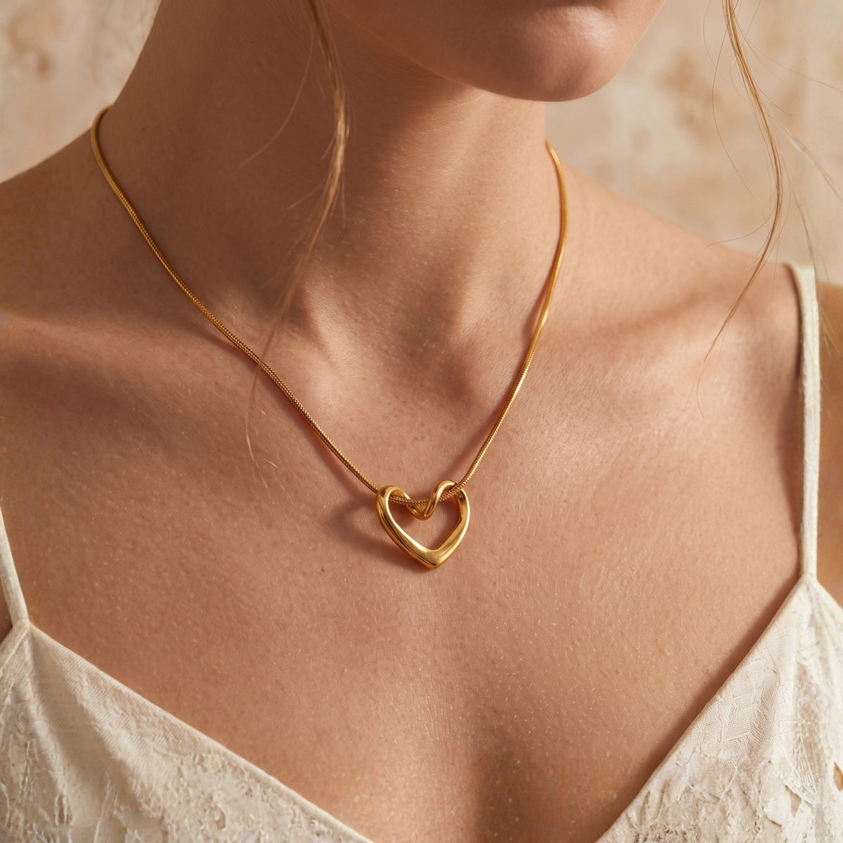Close-up view of the gold-tone fluid heart necklace worn around the neck with a white lace top.