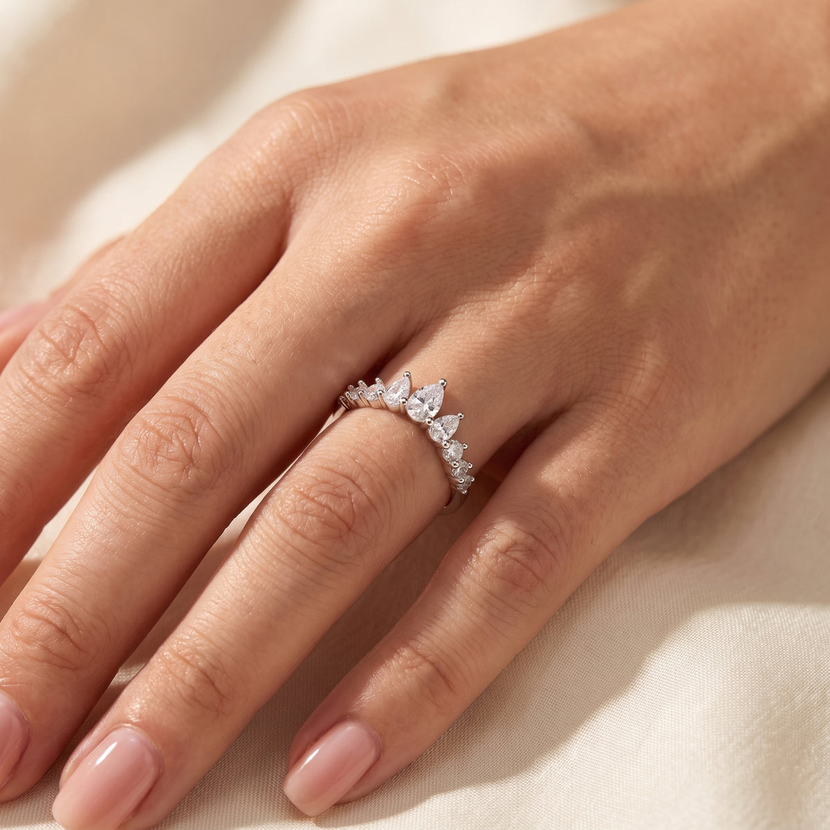 Silver pear tiara ring worn on a model's hand over cream fabric.