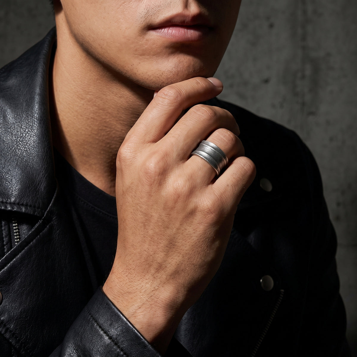 Silver ribbed open-band ring worn on a hand against a black leather jacket.