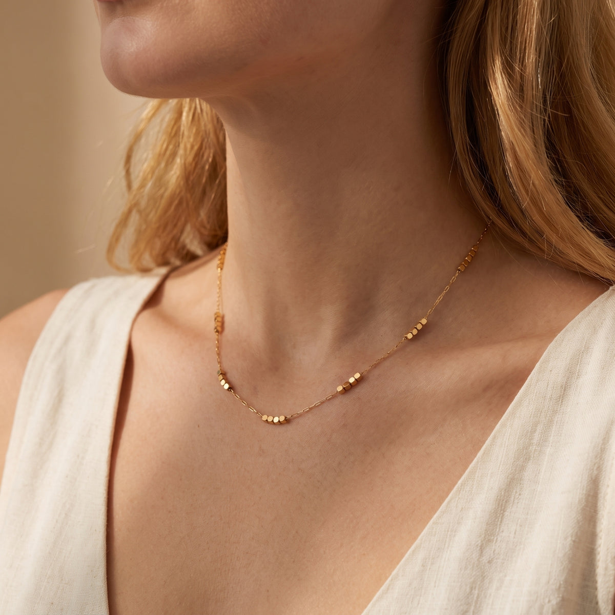 Model wearing the gold-tone station necklace with clustered cube beads and a light V-neck top.
