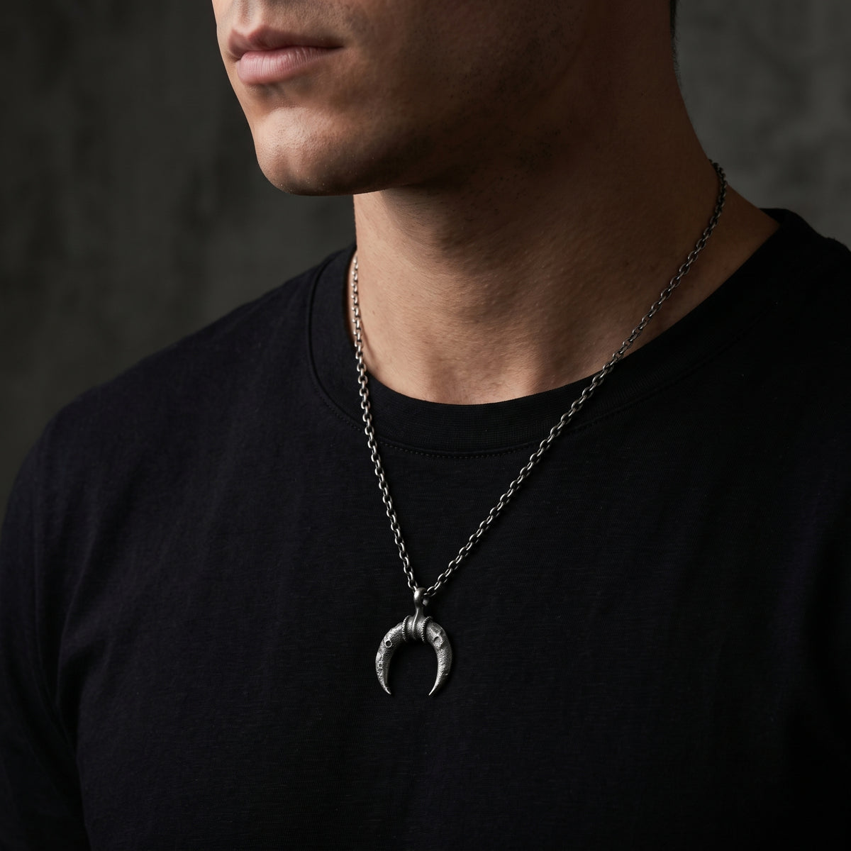 Side-angle view of a man wearing the crescent pendant necklace over a black T-shirt.