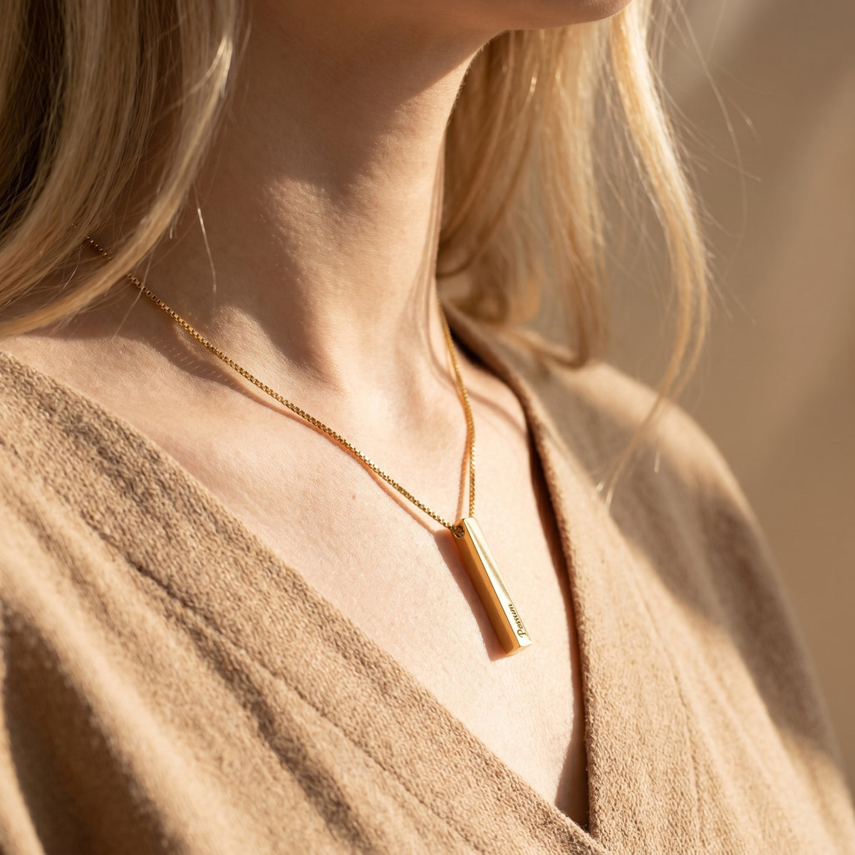 Model wearing the personalized gold bar necklace with a beige V-neck top.