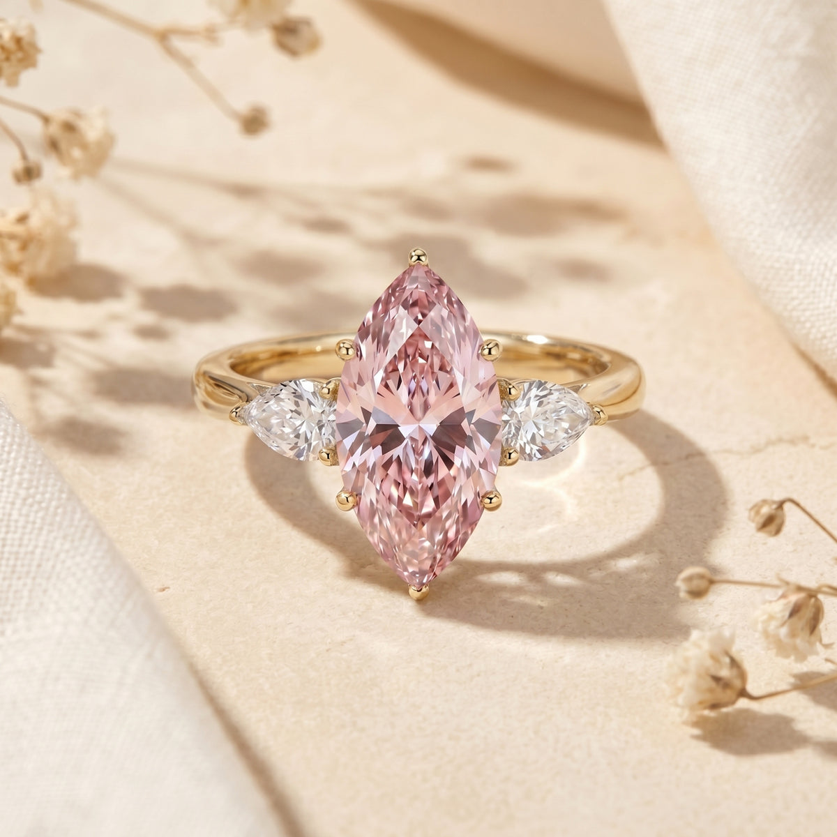 Marquise pink moissanite yellow gold promise ring with pear side stones on a lifestyle background.