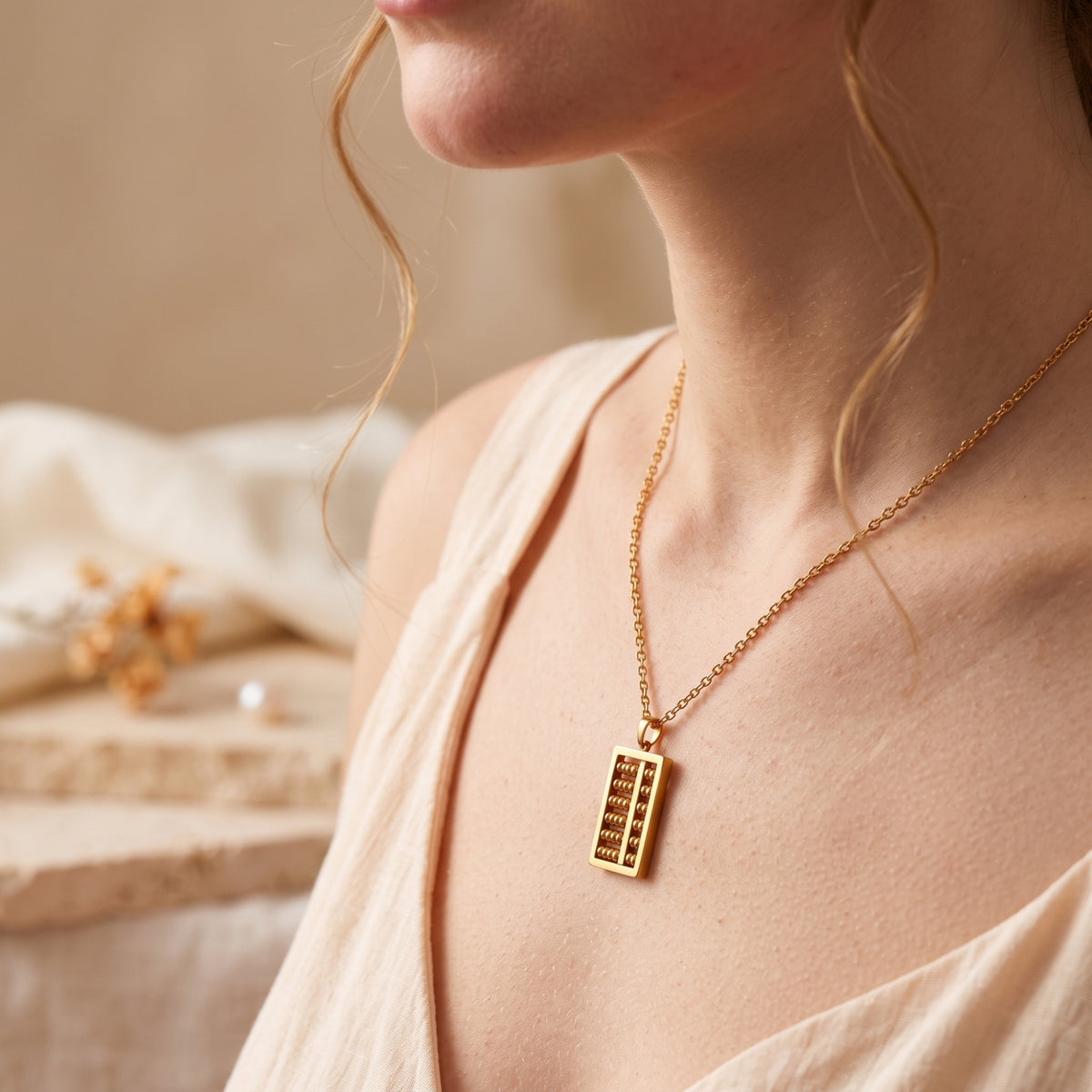 Model wearing the gold-tone abacus necklace with a cream-colored top, shown from a side angle.