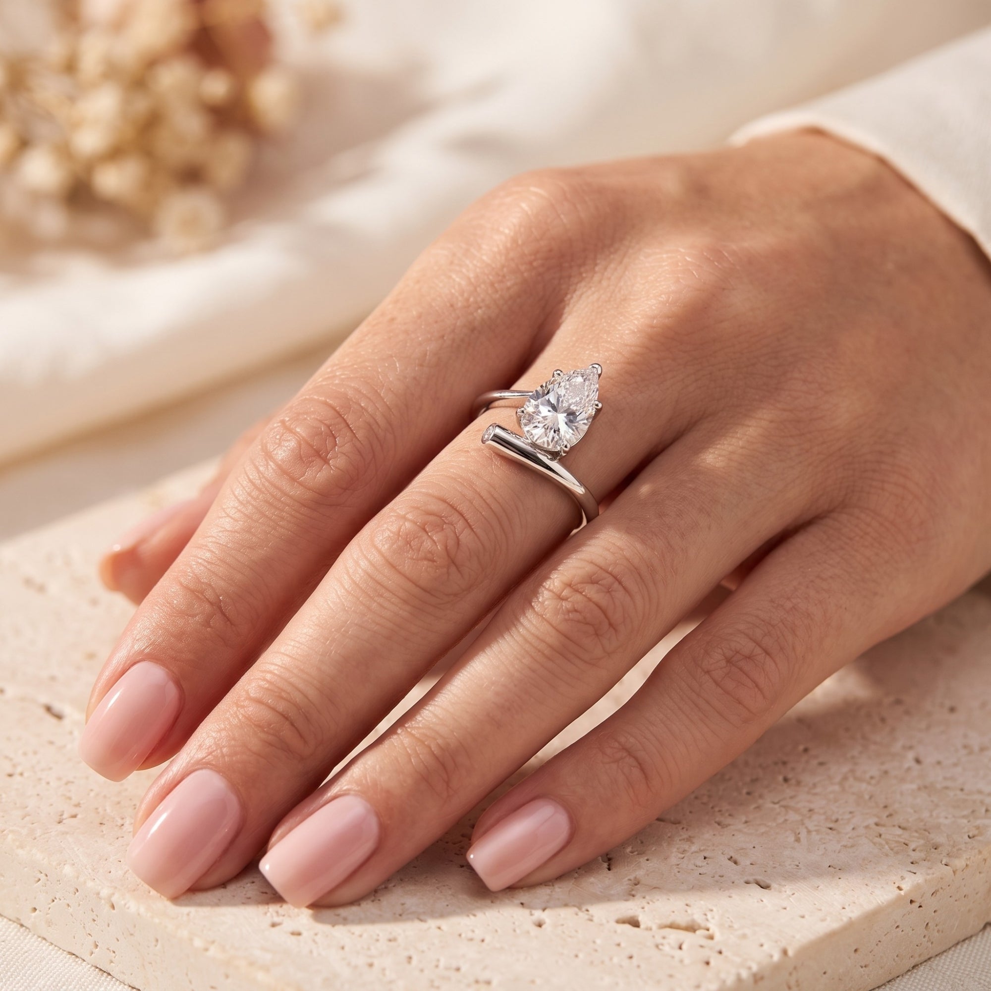 Sterling silver bypass ring with a pear-cut simulated diamond shown on a hand.