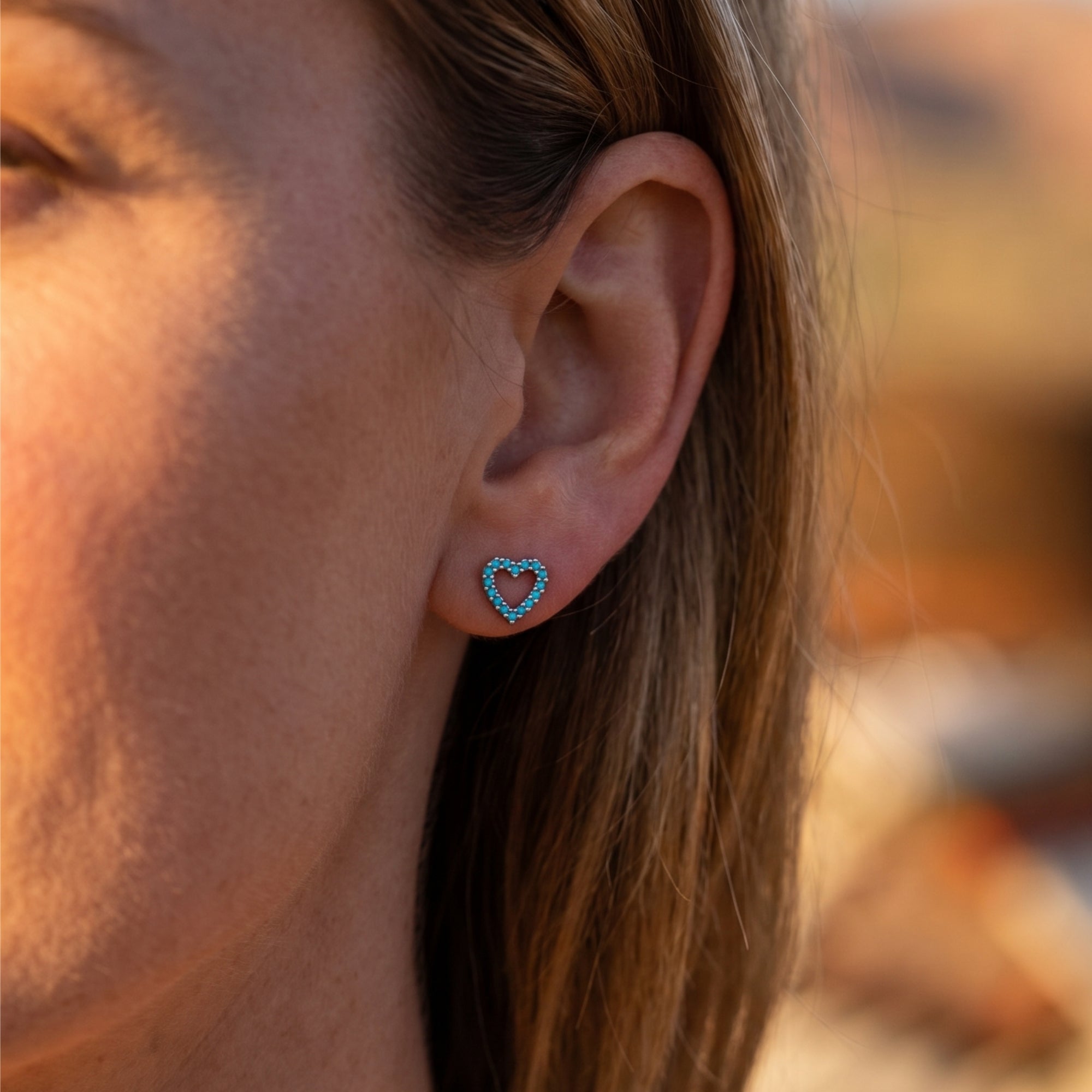Close-up of a silver heart-shaped turquoise earring worn on a woman's ear in natural sunlight.