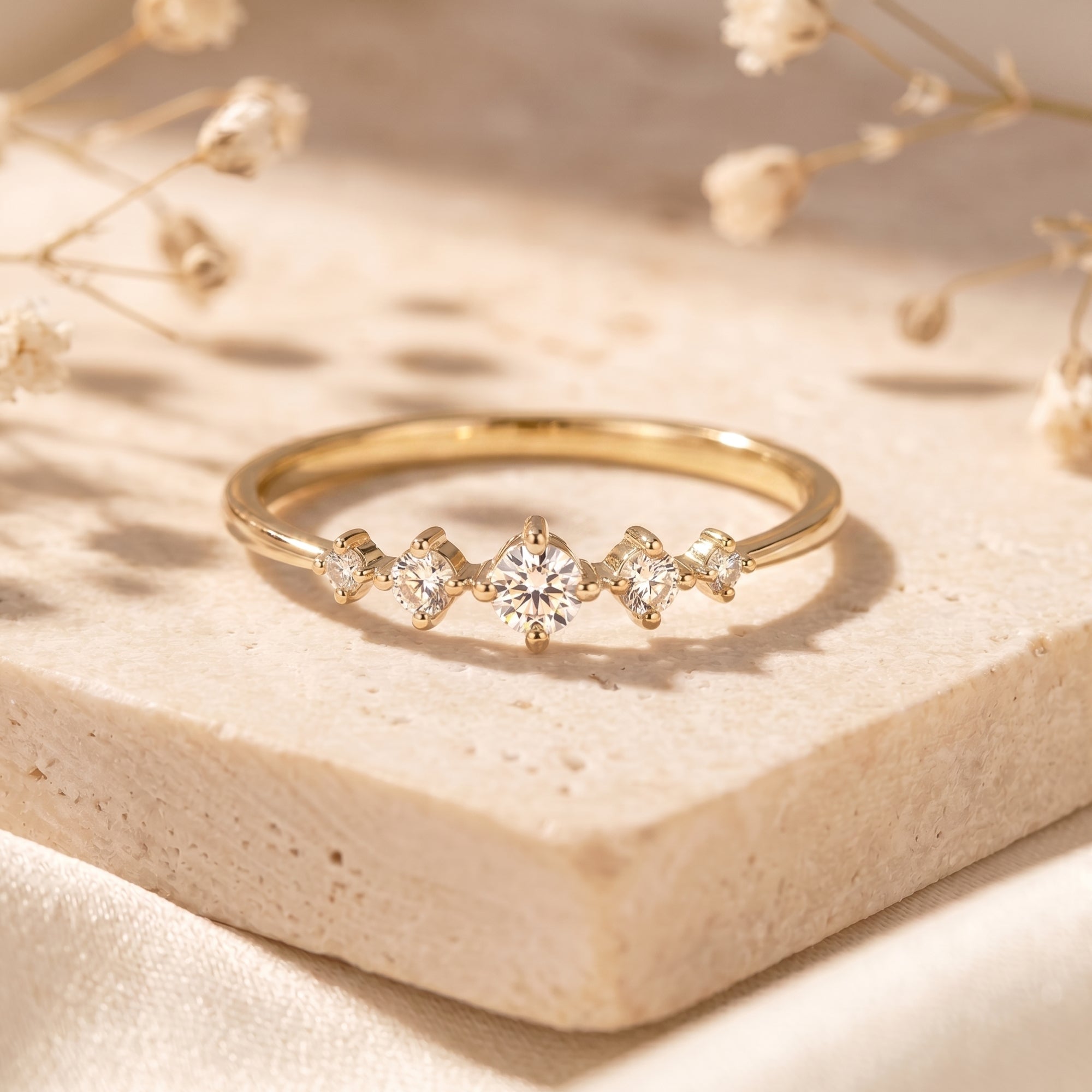 Gold moissanite ring with five round stones on a stone base.