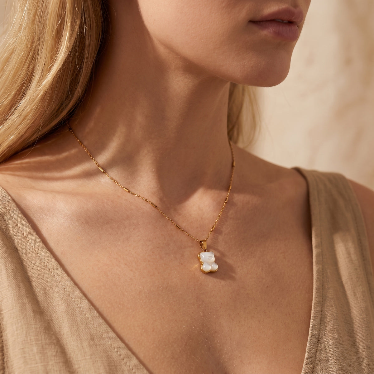 Side-angle close-up of a model wearing the gold-tone bear pendant necklace over a beige top.