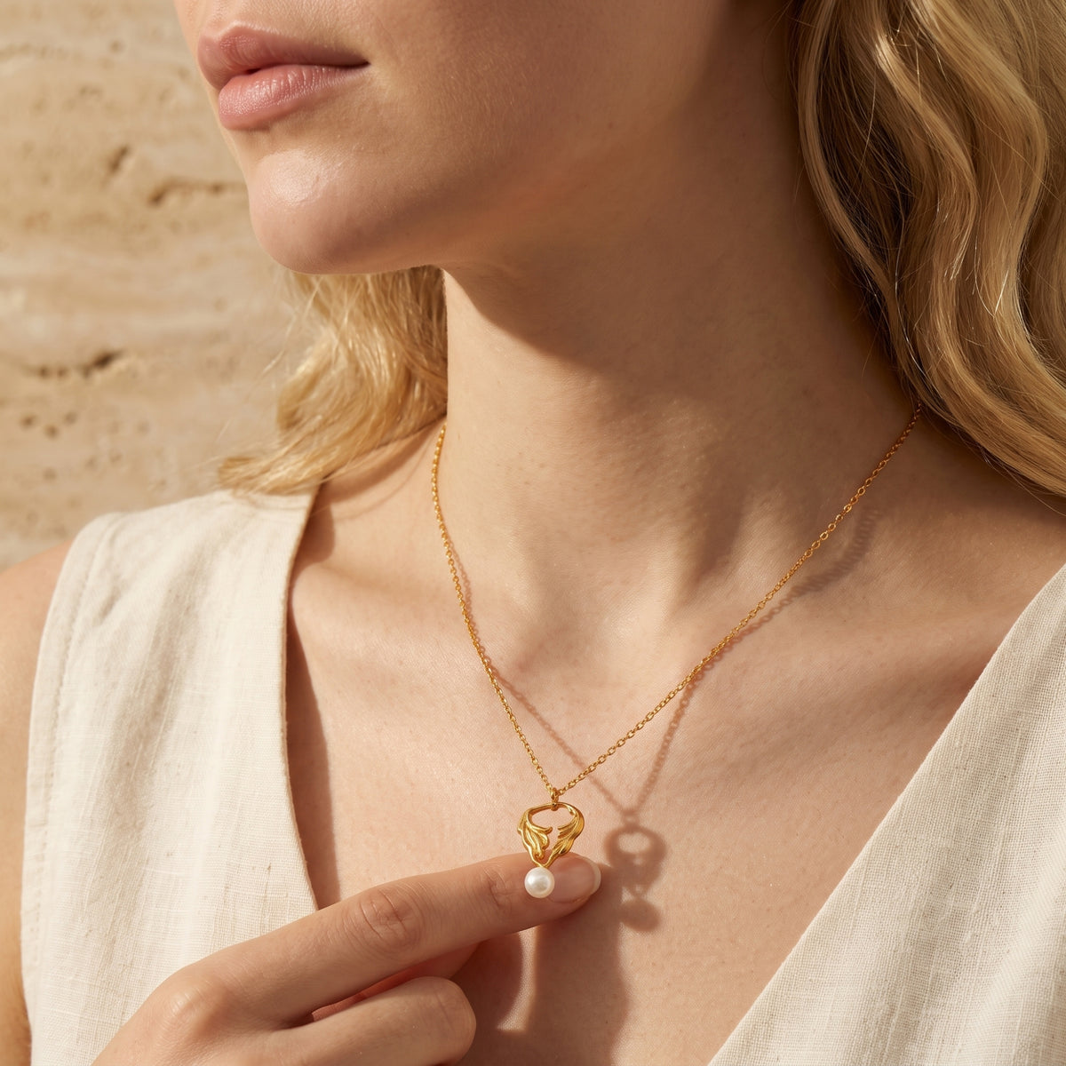 Close-up of a model touching the white pearl on the gold-tone leaf pendant worn around the neck.