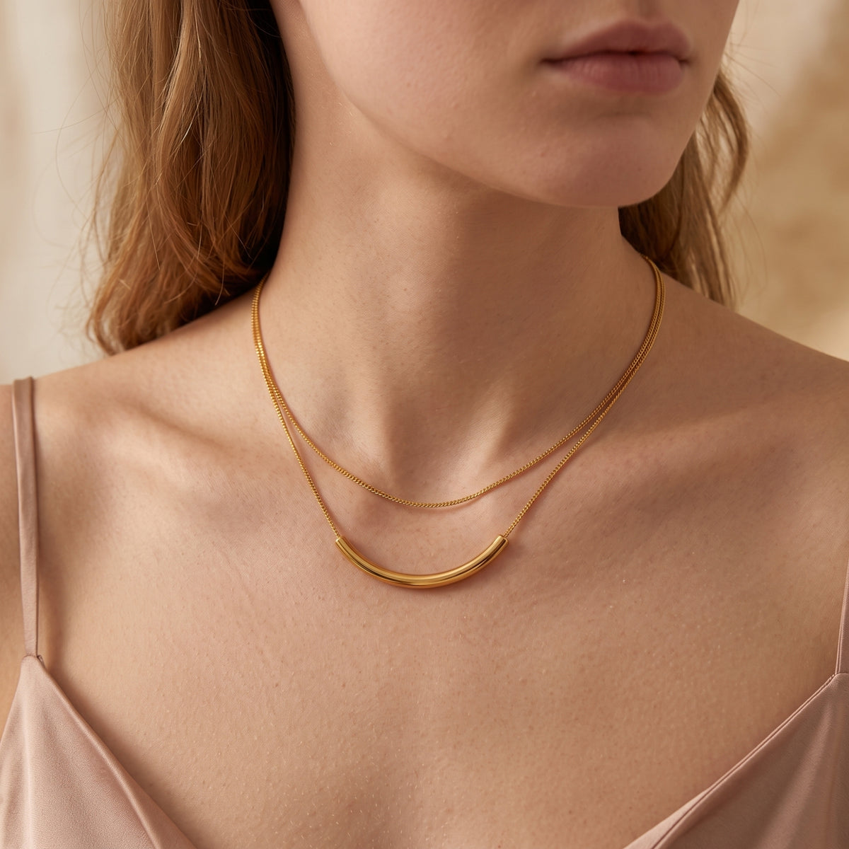 Model wearing the gold-tone double-strand necklace with a curved bar pendant, shown from the chest up.