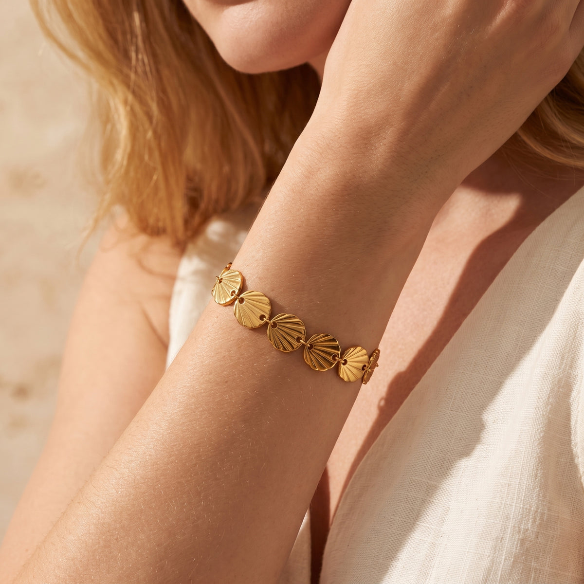Angled close-up of the gold-tone seashell link bracelet worn on a wrist beside white fabric