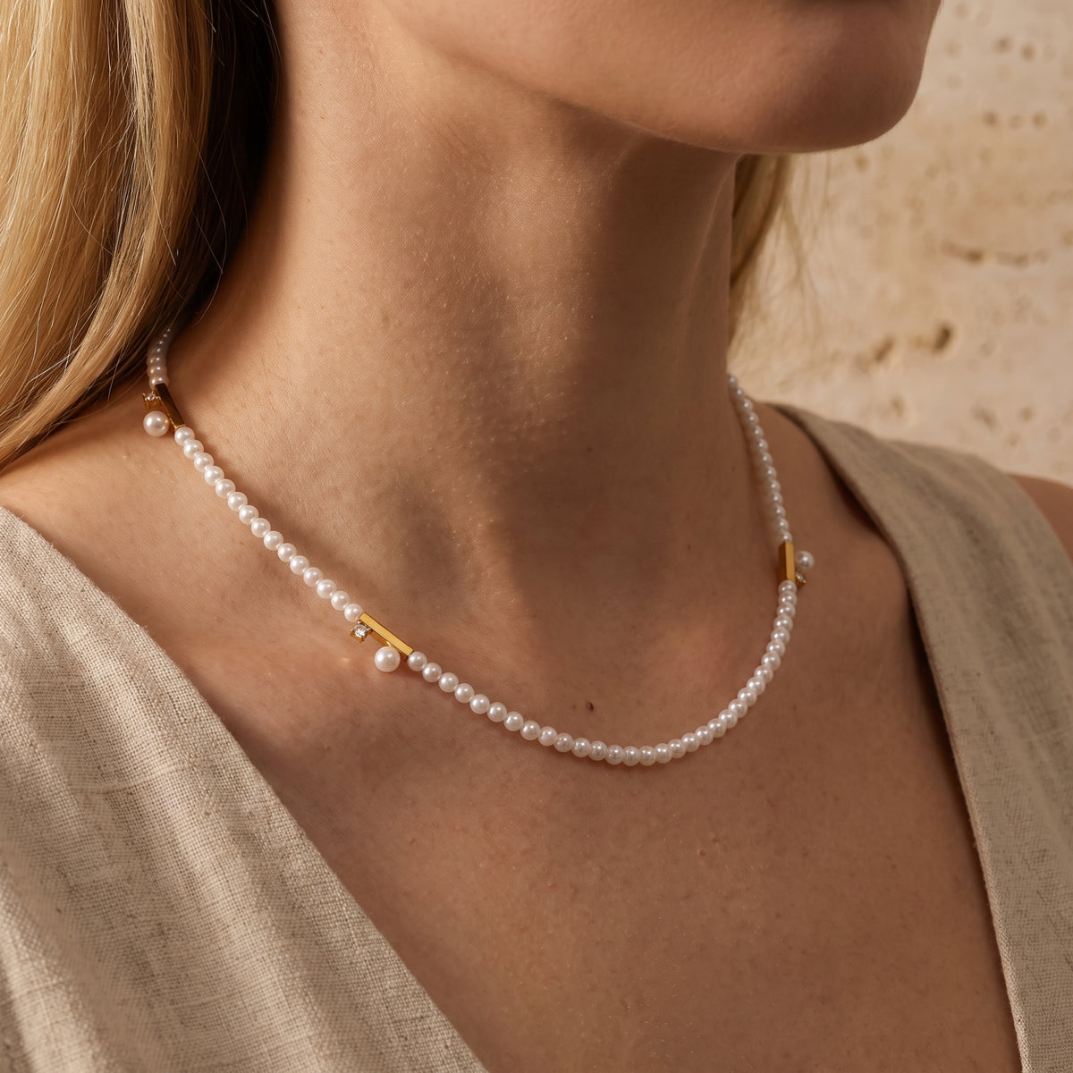 Angled close-up of a model wearing the gold-tone pearl bar station necklace with a beige linen top.