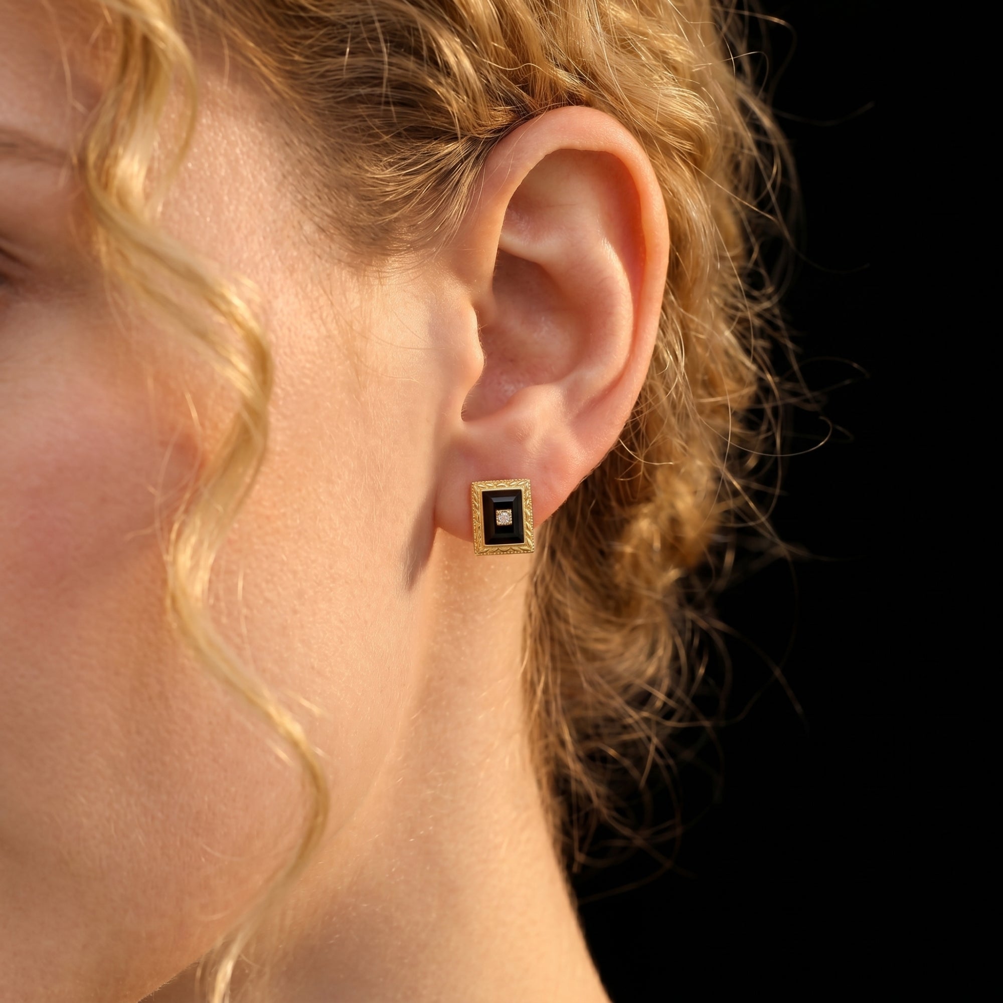 Close-up of a yellow gold square-cut black onyx earring with a center stone worn on a model's ear.