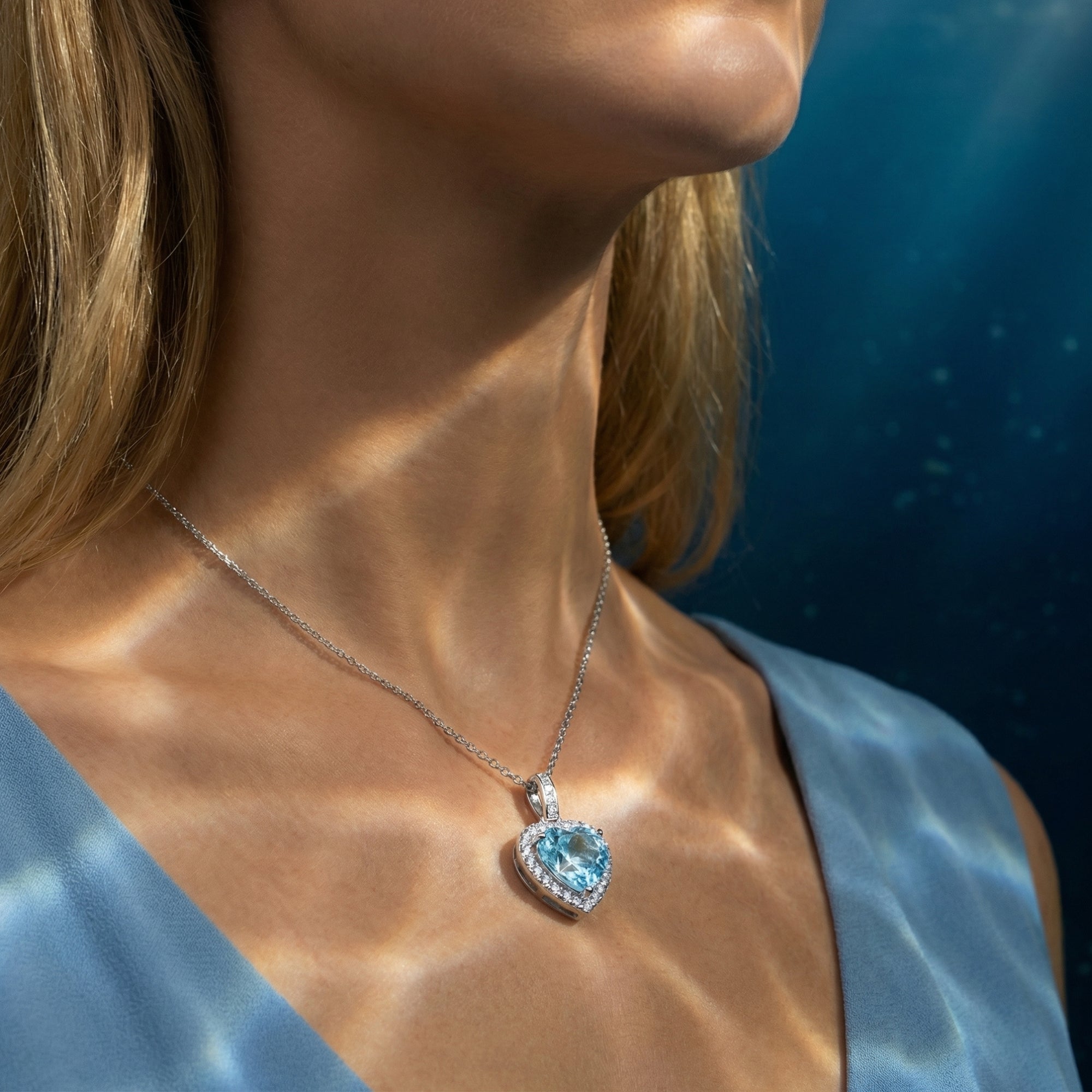 Side view of a woman wearing the platinum heart-cut natural aquamarine halo necklace against a blue dress.