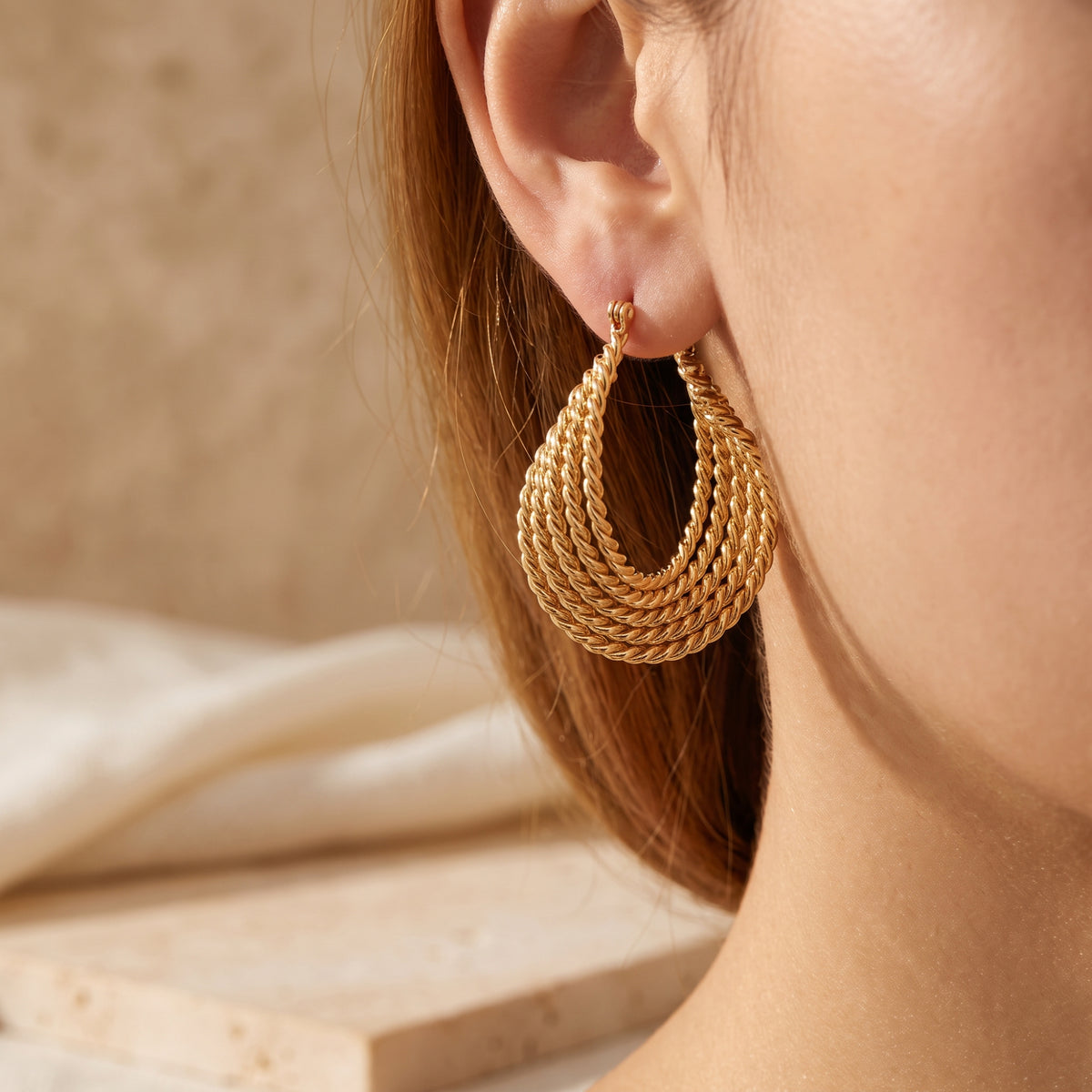 Close three-quarter view of a model wearing matching gold-tone multi-strand twisted rope drop earrings.