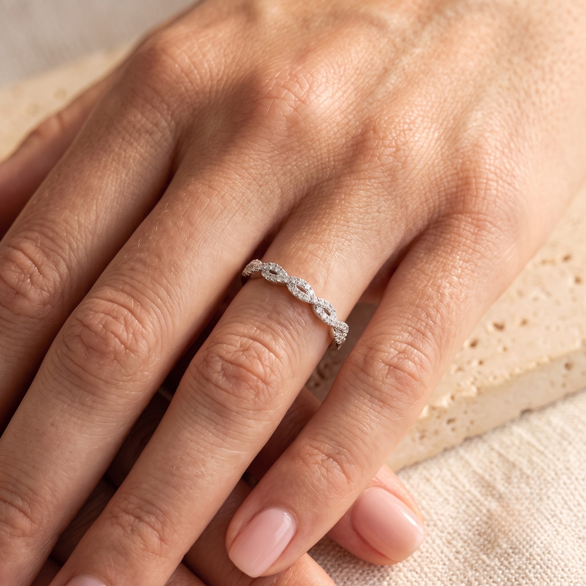 Helena twisted silver eternity ring with simulated diamonds on a model's hand against a neutral background.