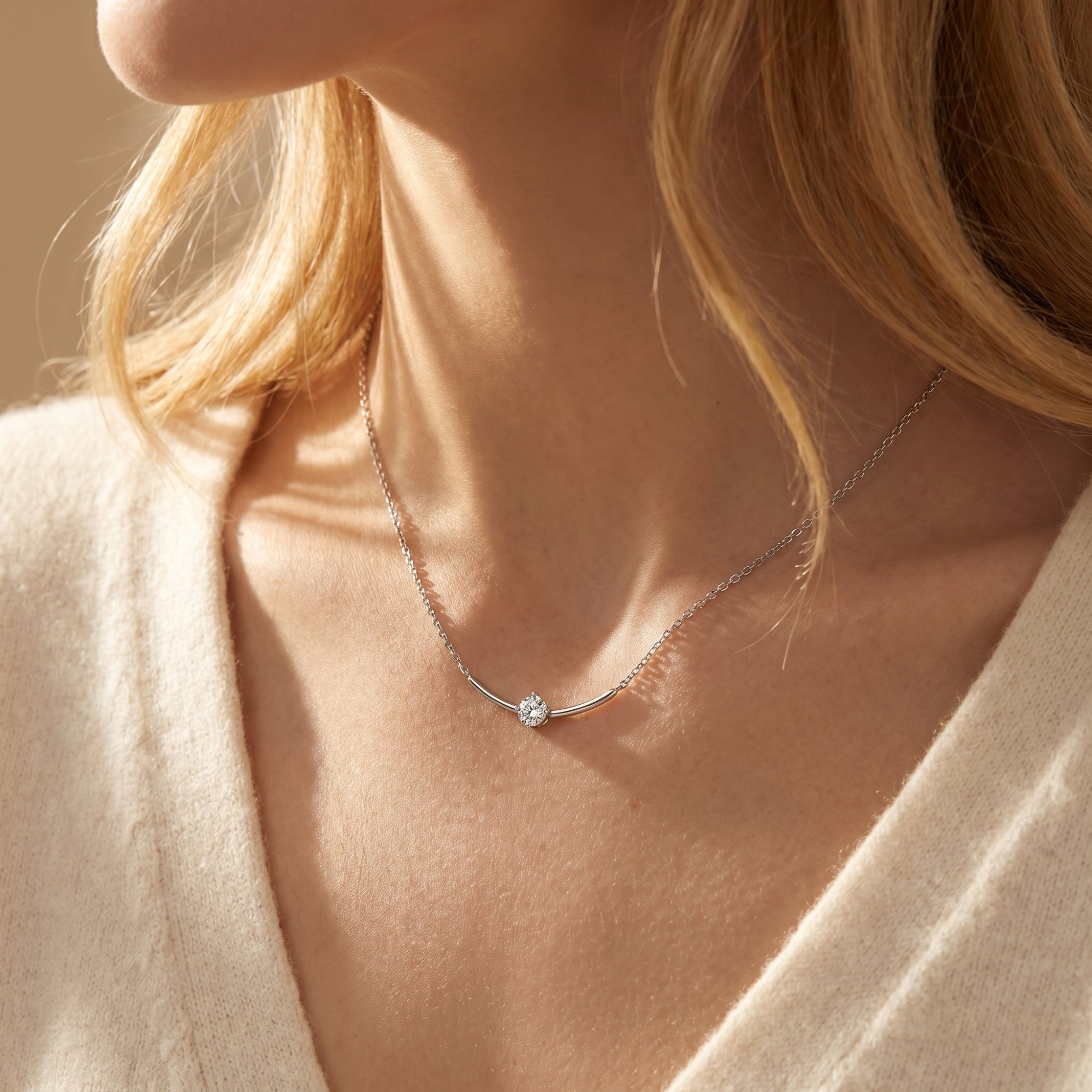 Close-up of a woman wearing the silver Elionara moissanite necklace with a round stone and curved bar.