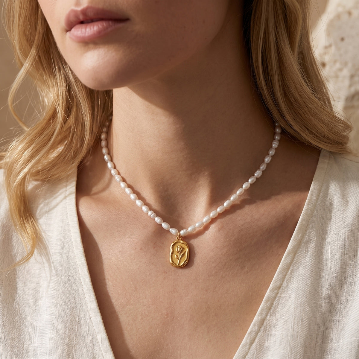 Front view of a model wearing the Rosalinde pearl necklace with a gold finish rose pendant.