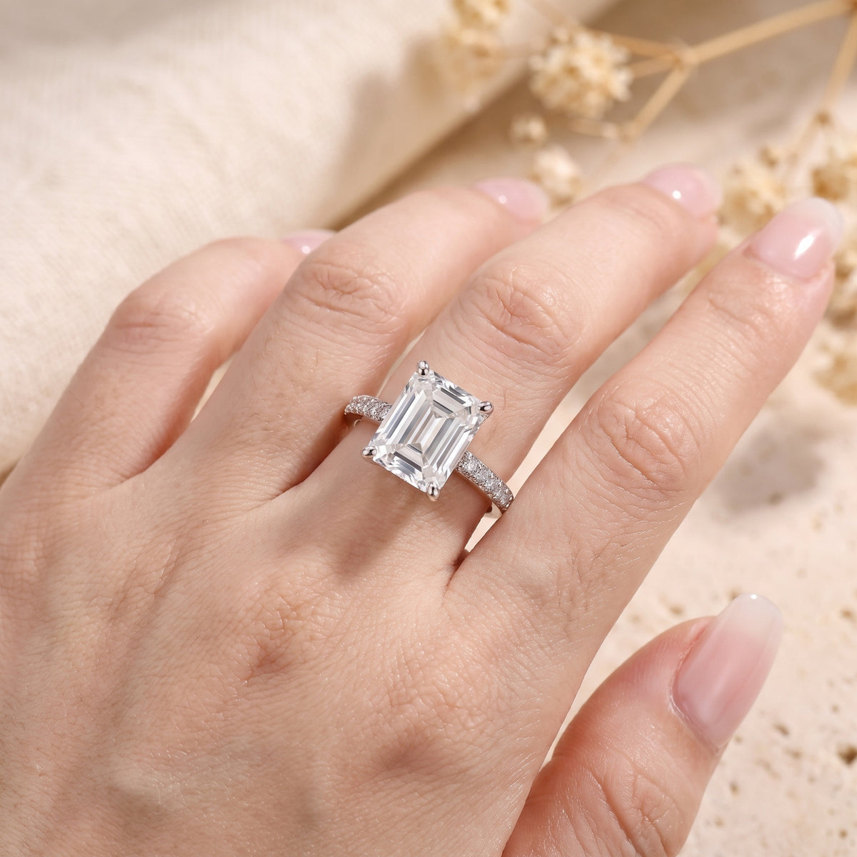 Angled view of a silver emerald-cut solitaire ring with pave accent stones worn on a hand.