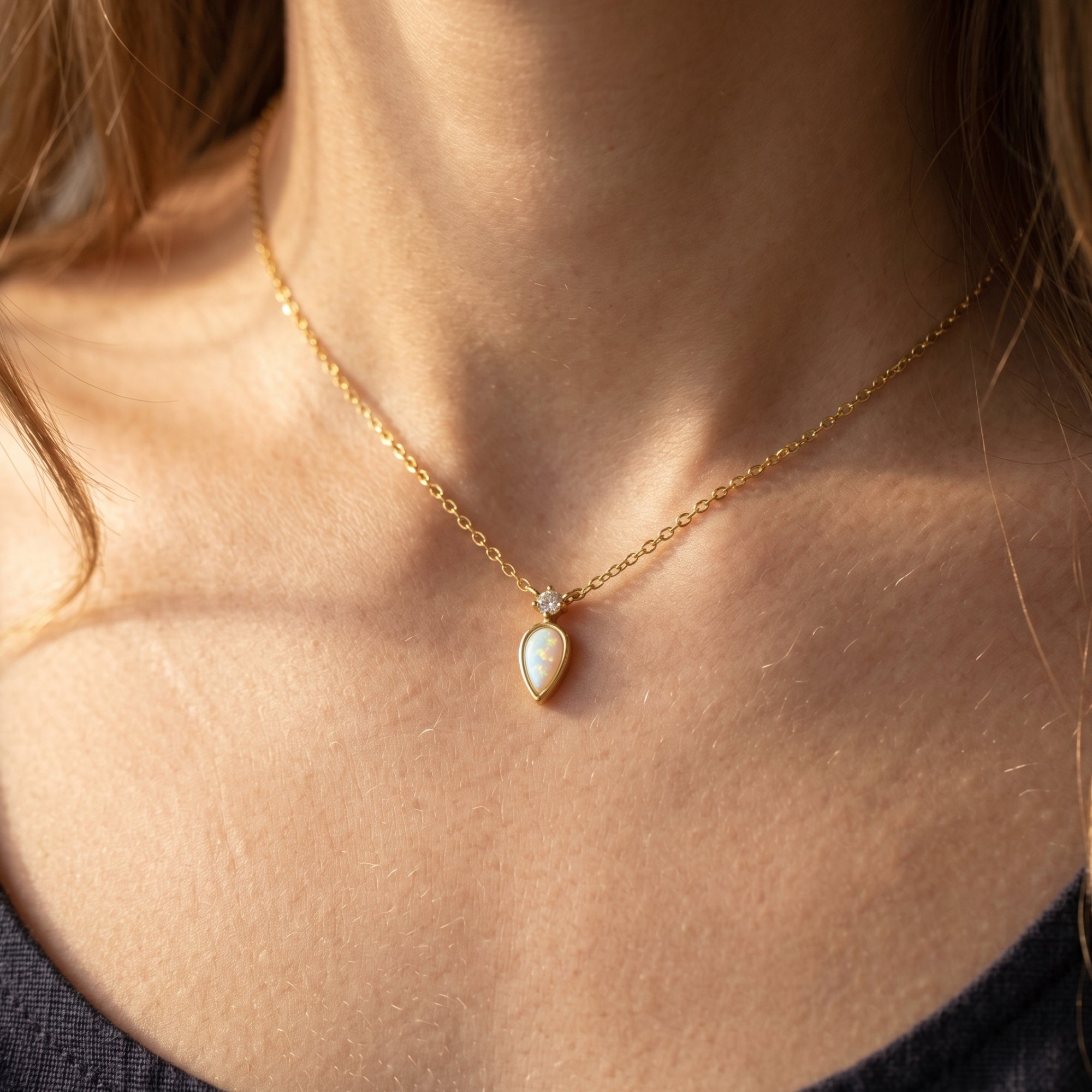 Close-up of a woman wearing the gold teardrop white opal necklace with a small diamond accent.