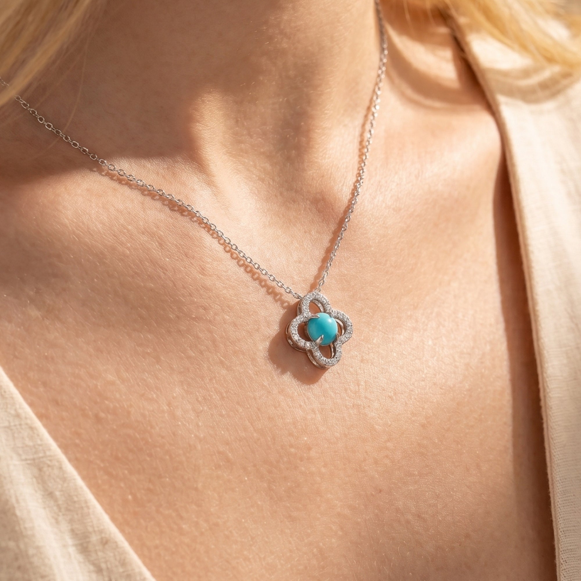Close-up of a silver quatrefoil necklace with a round turquoise centerpiece on a model.