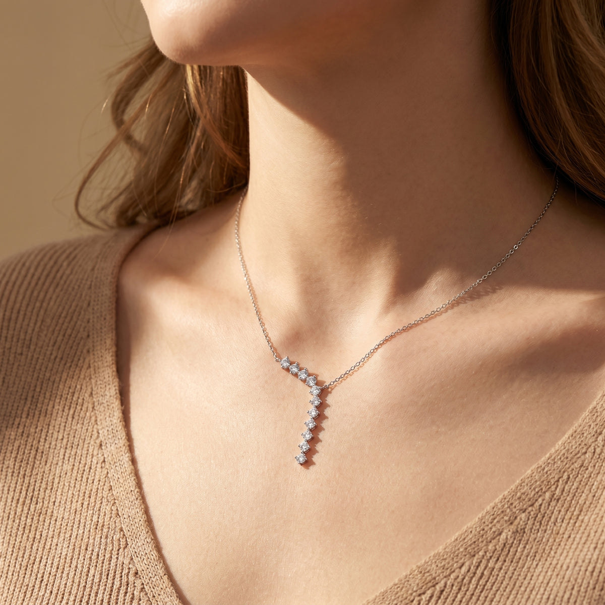 Silver curved drop necklace with round-cut moissanite stones worn by a model in a tan sweater.