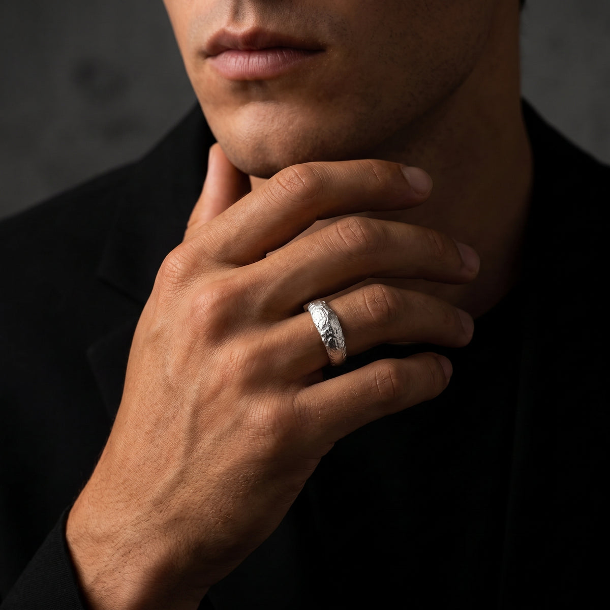 Model wearing a textured silver open ring on his ring finger with his hand resting beneath his chin.