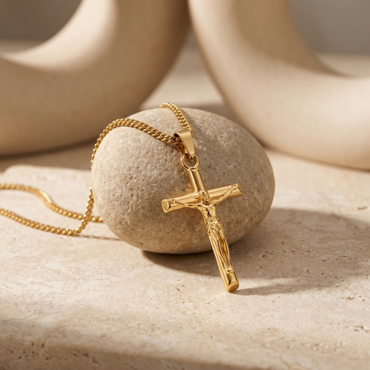 Close-up of a gold crucifix pendant and chain draped over a round textured stone on a light stone surface.