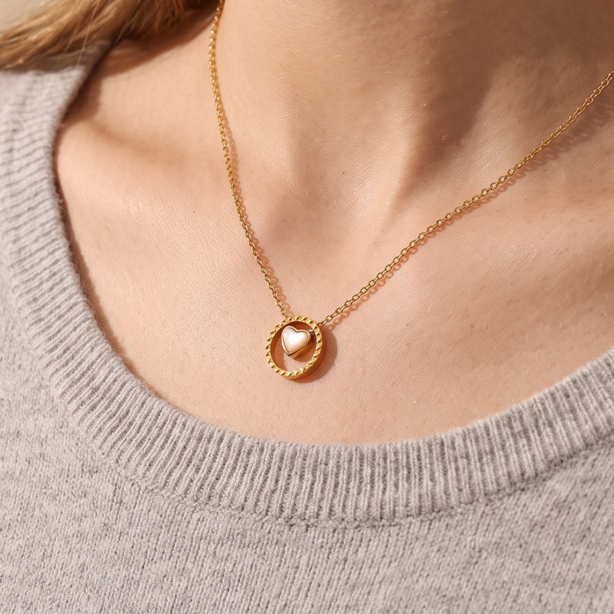 Gold Rosetta mother of pearl heart necklace worn with a grey knit sweater.
