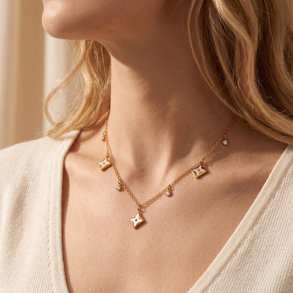 Gold finish statement necklace with white star pendants and crystals styled on a model wearing a V-neck top.