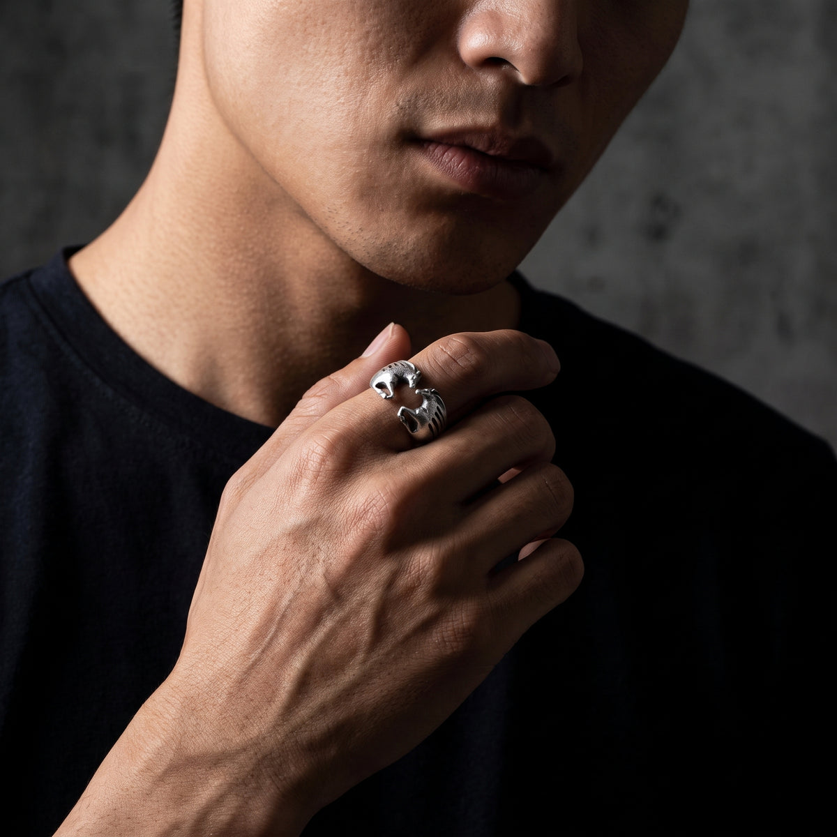 Man wearing the silver dual horse open ring on his index finger with his hand raised near his collarbone.