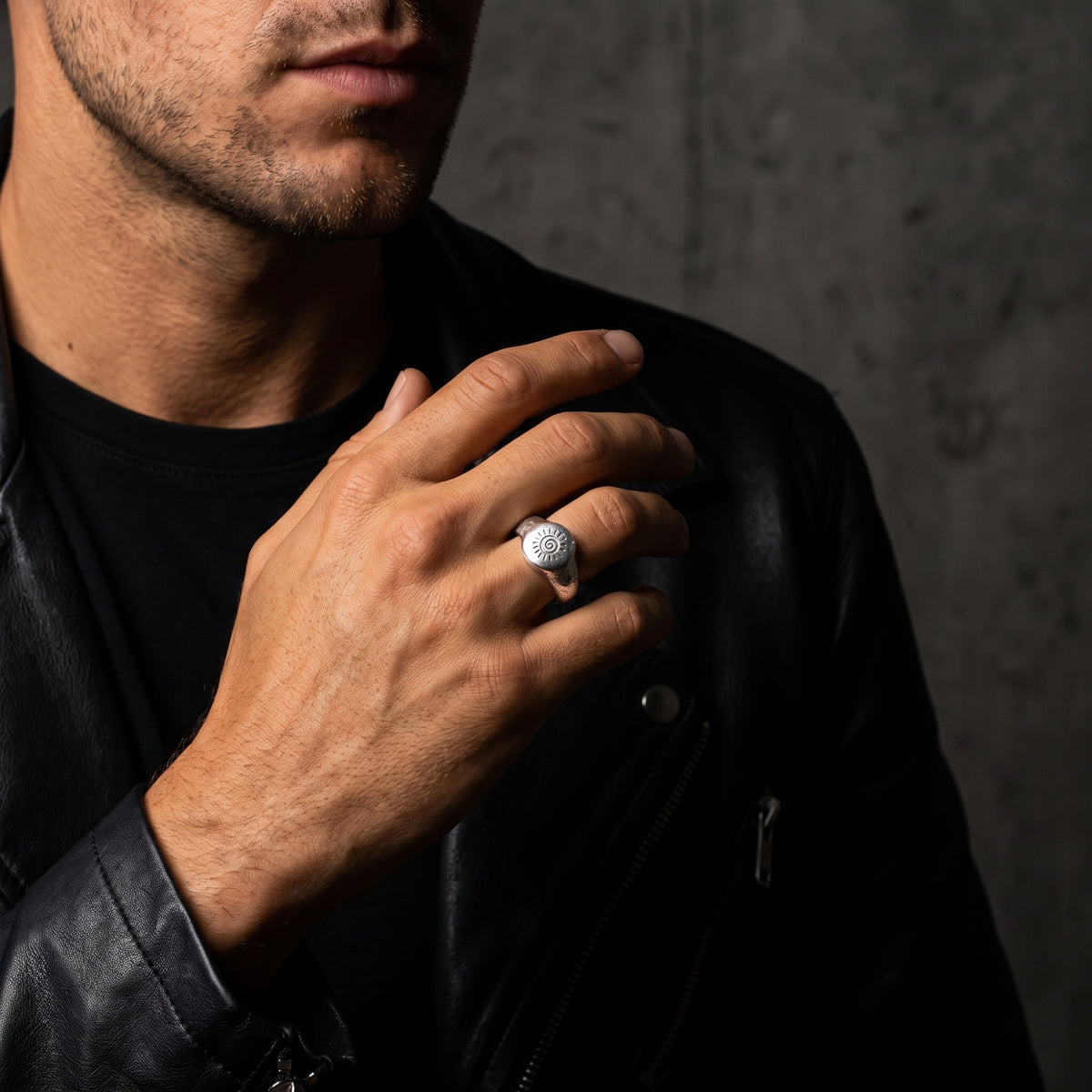 Model wearing the silver solar spiral signet ring across his chest over a black leather jacket.