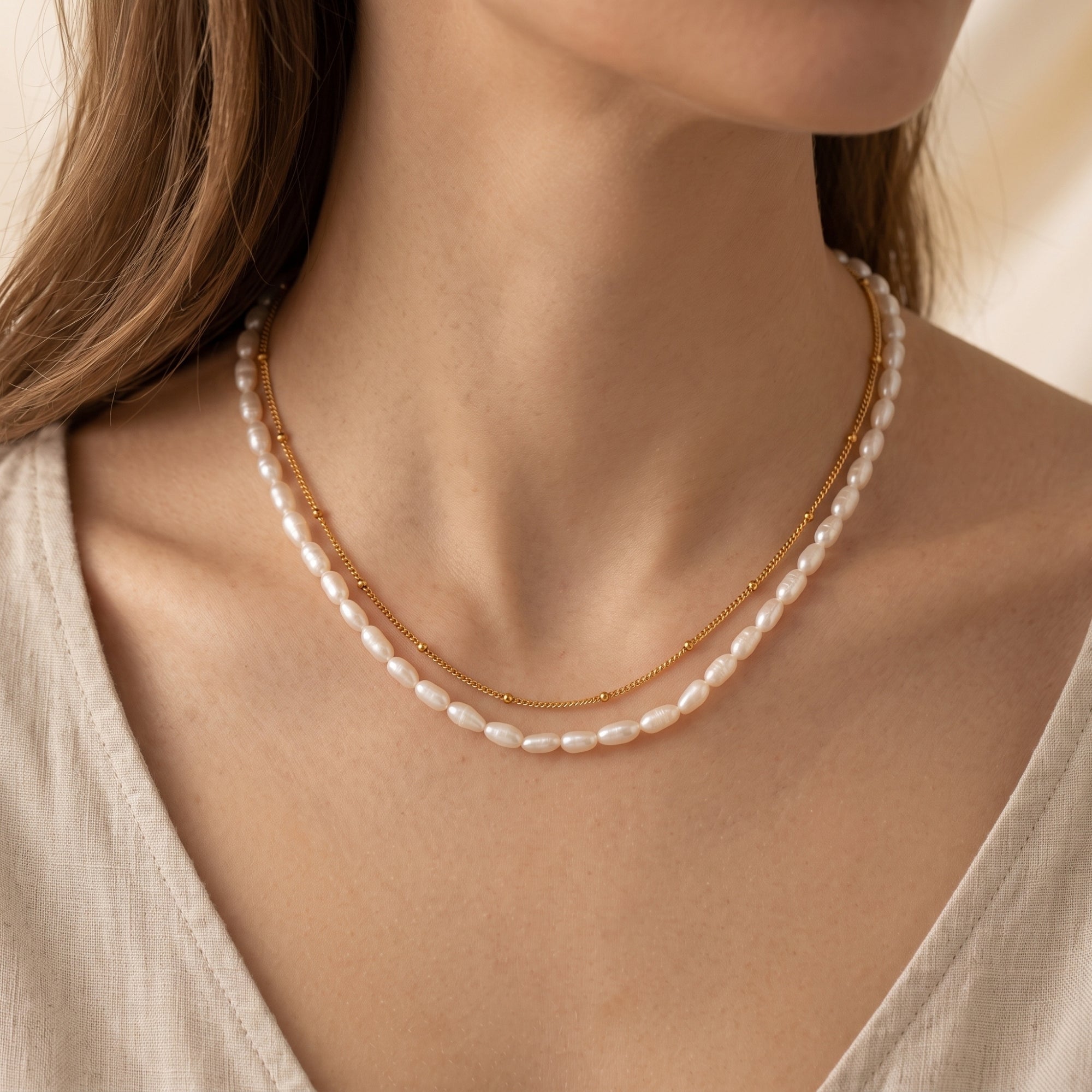 Double-layered gold and freshwater pearl necklace worn by a woman against a neutral top.