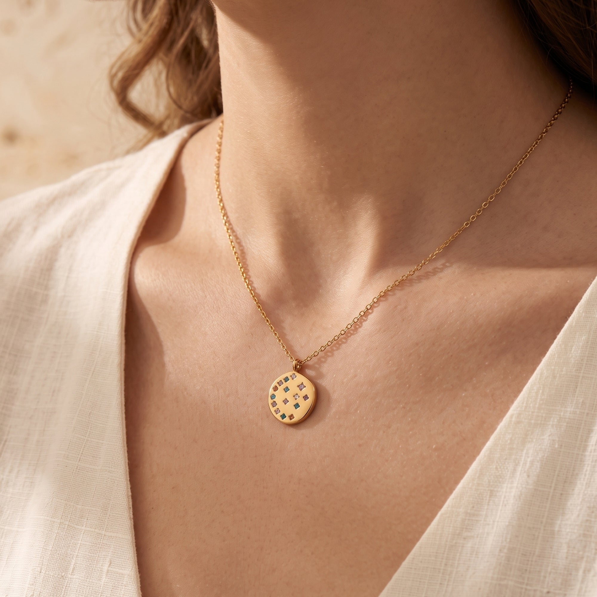 18K gold Astraline pendant necklace with multi-color crystals worn by a model in a cream-colored top.