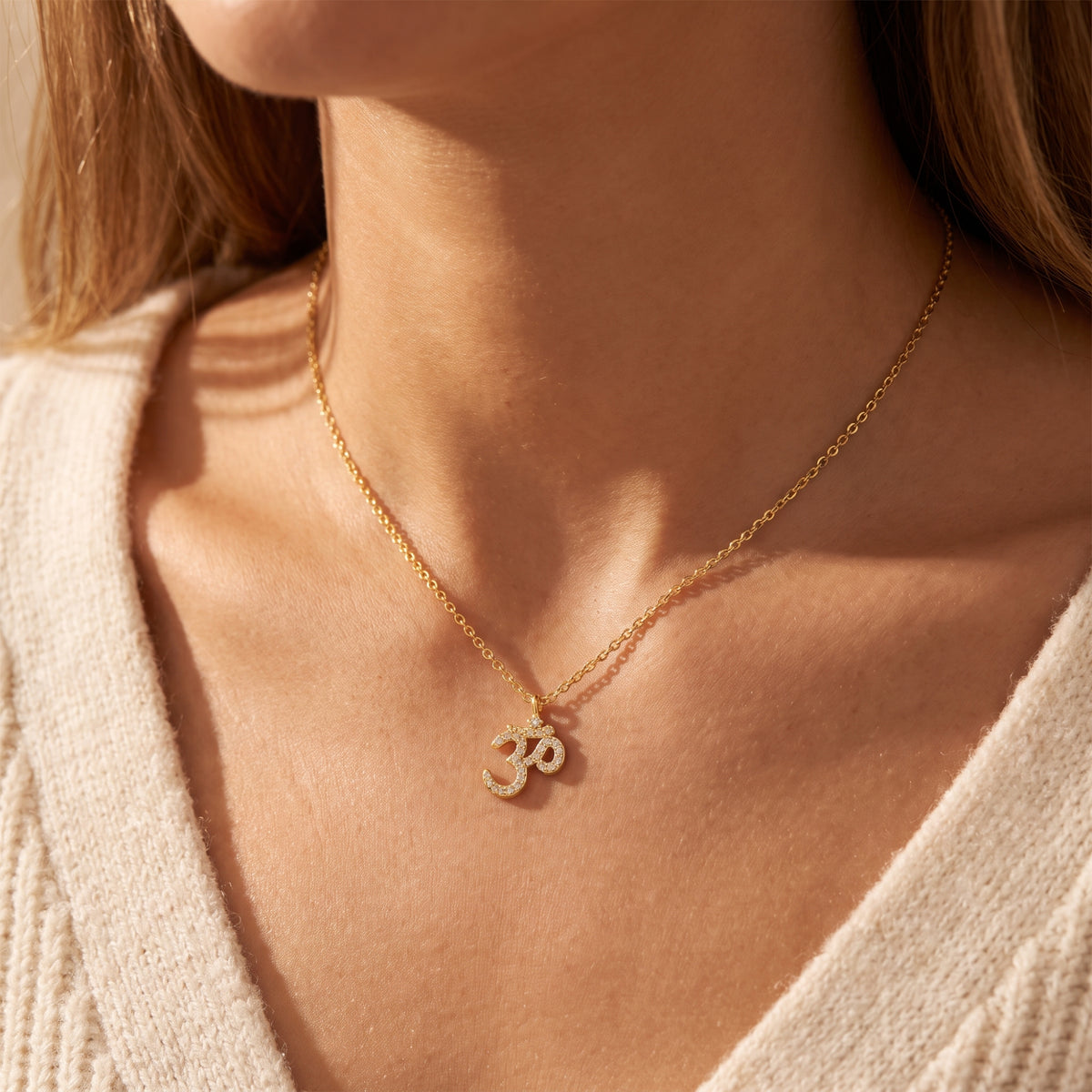 Close-up of a model wearing the gold-tone pave Om pendant necklace paired with a cream sweater.