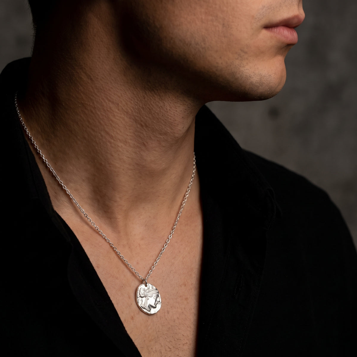 Side view of a man wearing the silver Athenian coin pendant necklace with an open black shirt.