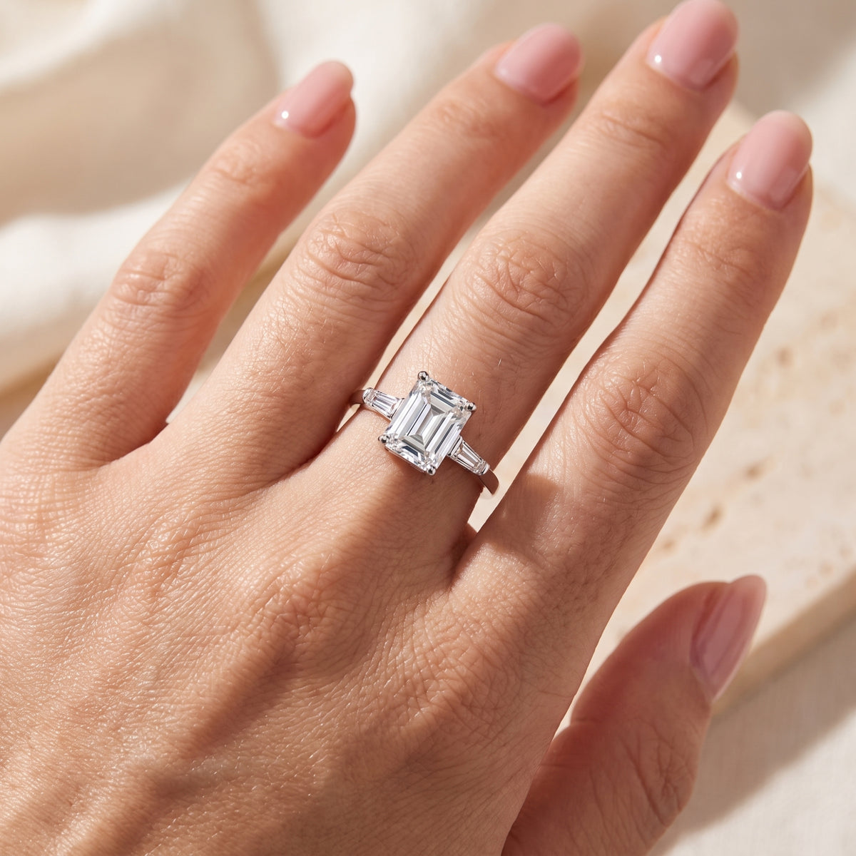Overhead view of a hand displaying a silver three-stone ring with an emerald-cut center stone.
