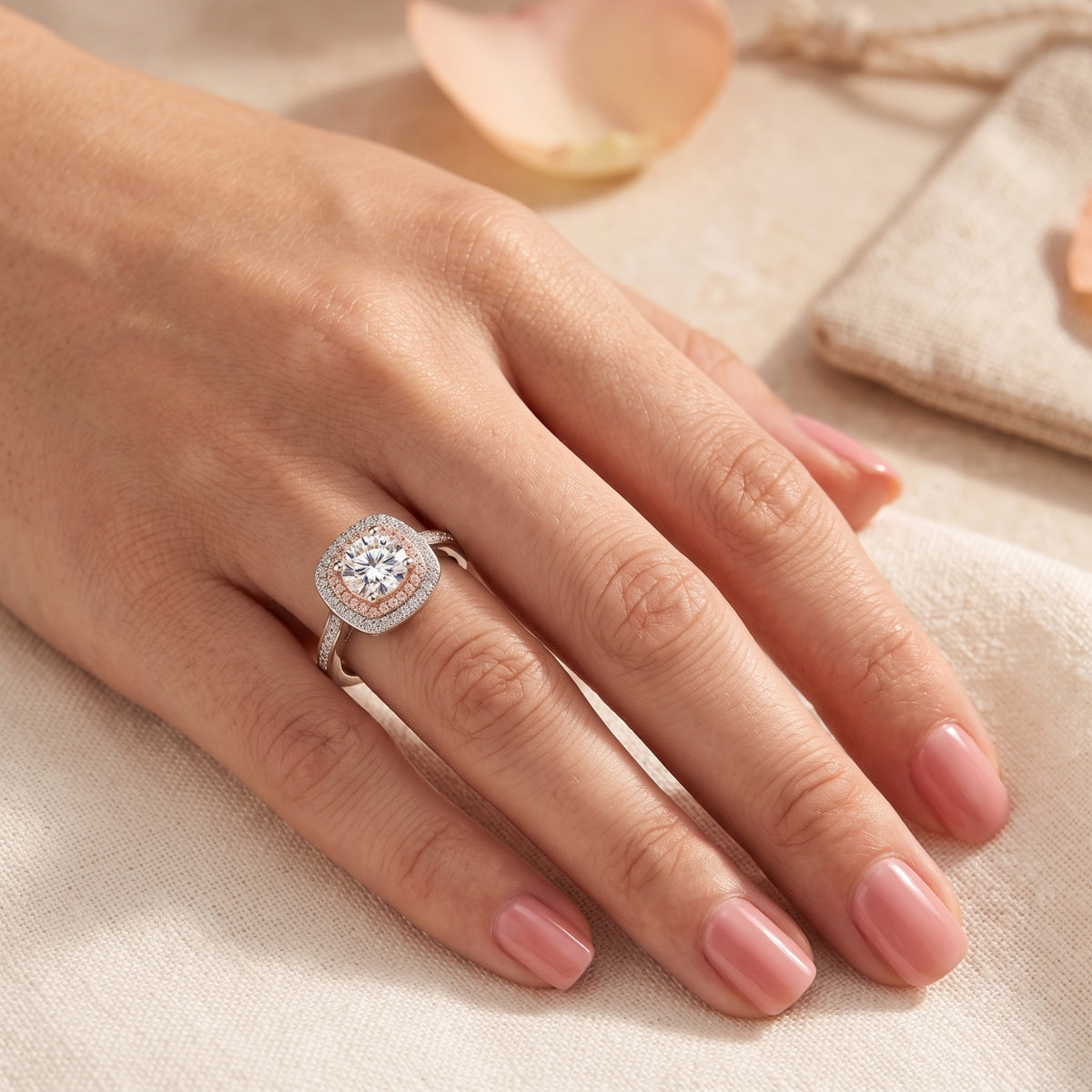 Hand wearing the dual-halo ring with pink inner accents on beige fabric.