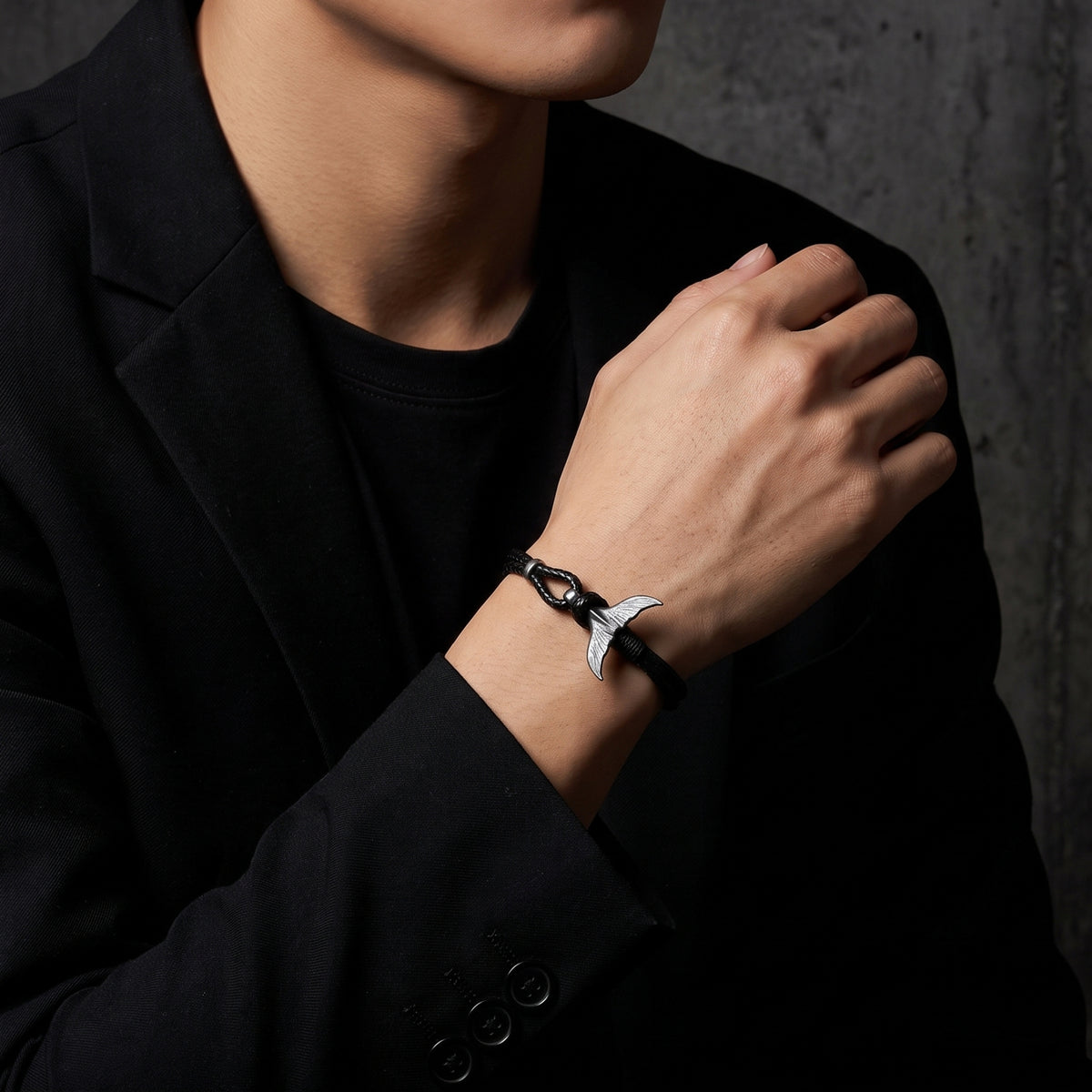Model wearing the black cord bracelet with a silver whale tail clasp over a black blazer.