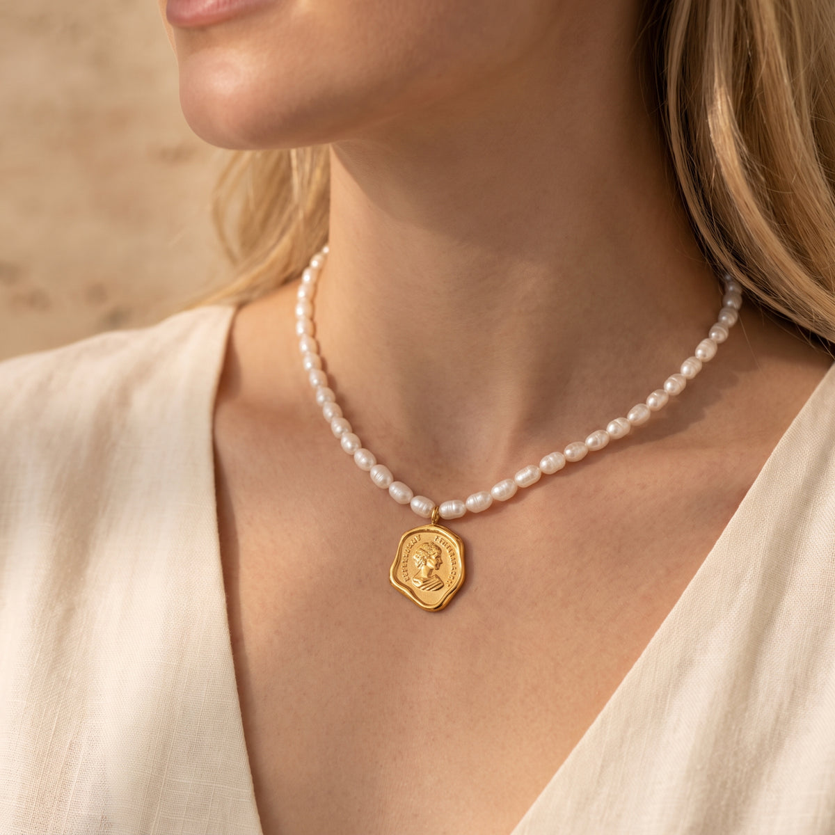 Angled close-up of a model wearing white pearl-inspired beads with a gold-tone coin medallion pendant.