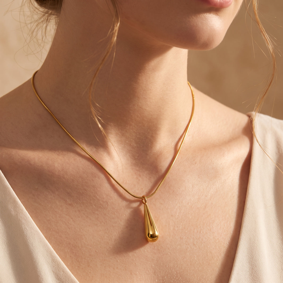 Angled close-up of a model wearing a polished gold-tone teardrop pendant necklace on her chest.