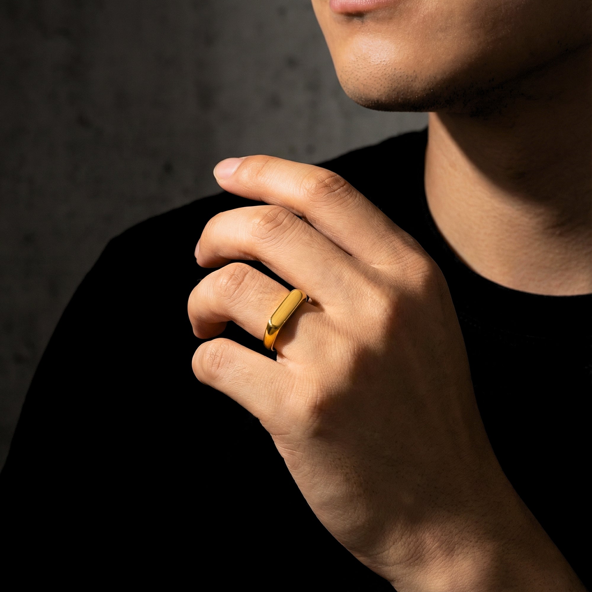 Close-up of a man's hand wearing the gold stainless steel Pillar signet ring against a dark background.