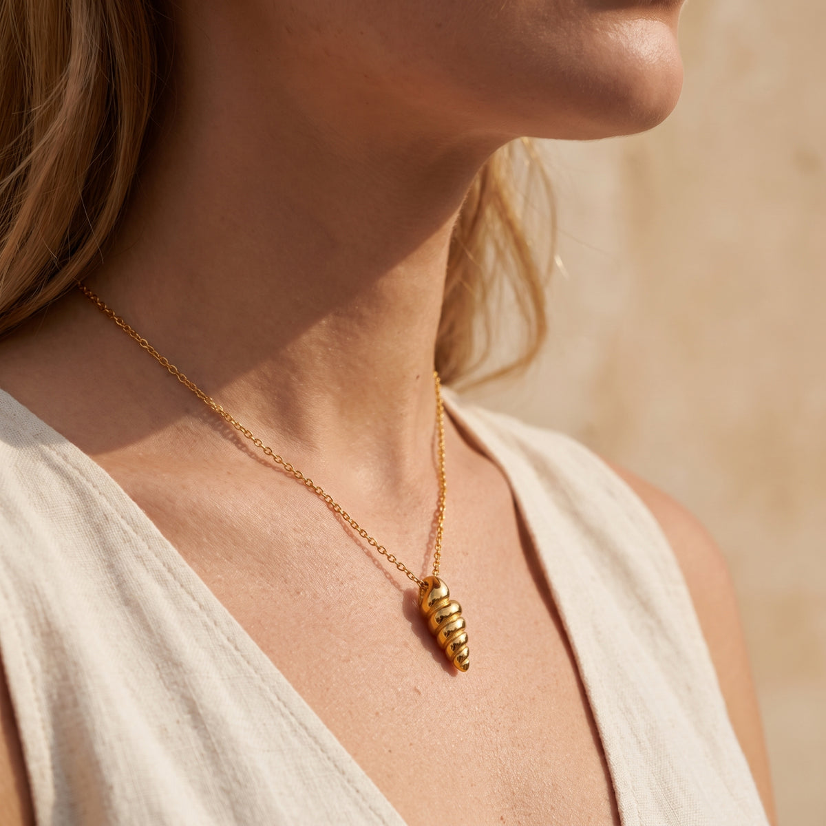 Side-angle view of a model wearing the gold-tone spiral shell necklace in sunlight.