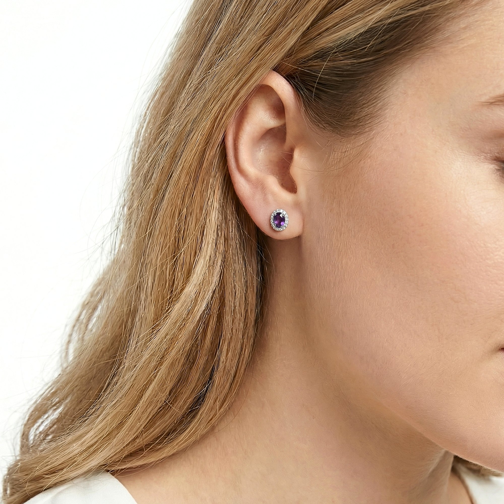 Close-up of a woman wearing an oval purple amethyst halo stud earring in sterling silver.