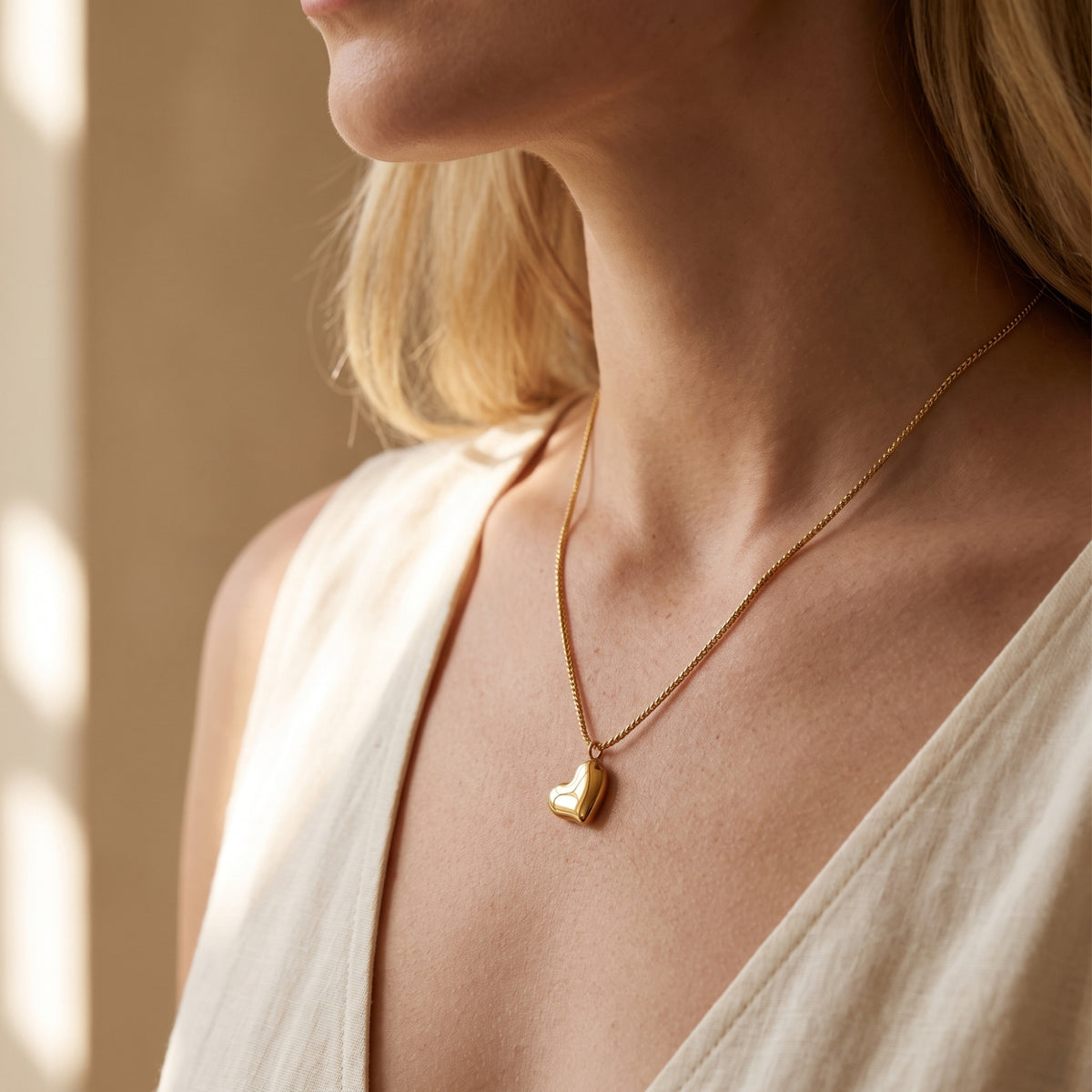 Three-quarter view of a model wearing the gold-tone puffed heart pendant necklace against a light garment.